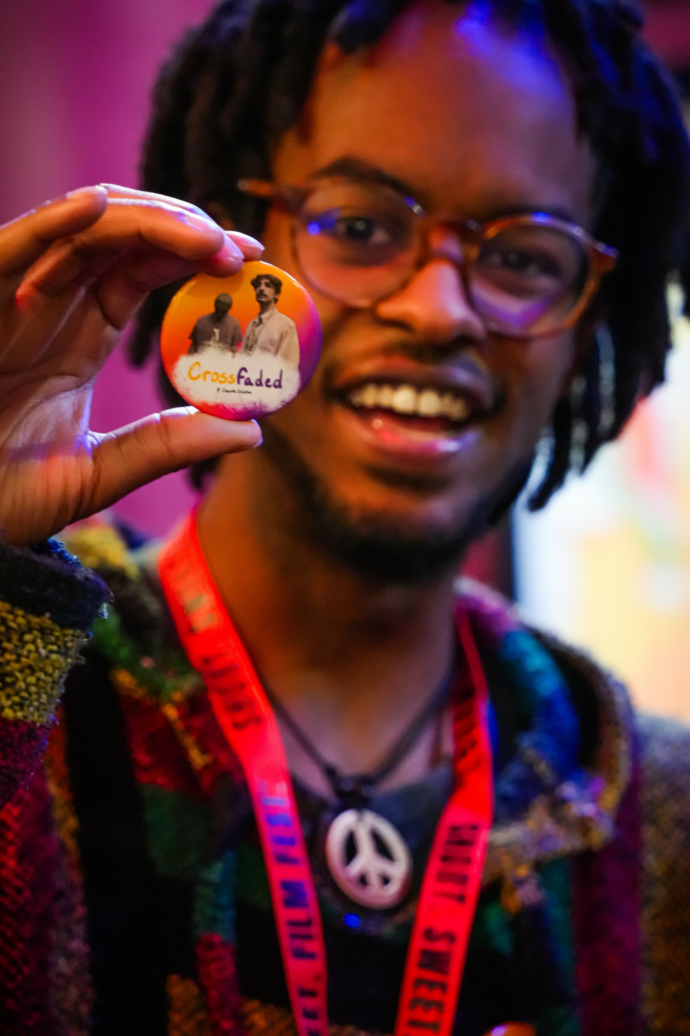 Person with glasses holding a badge with a logo and a person image, smiling, colorful background.