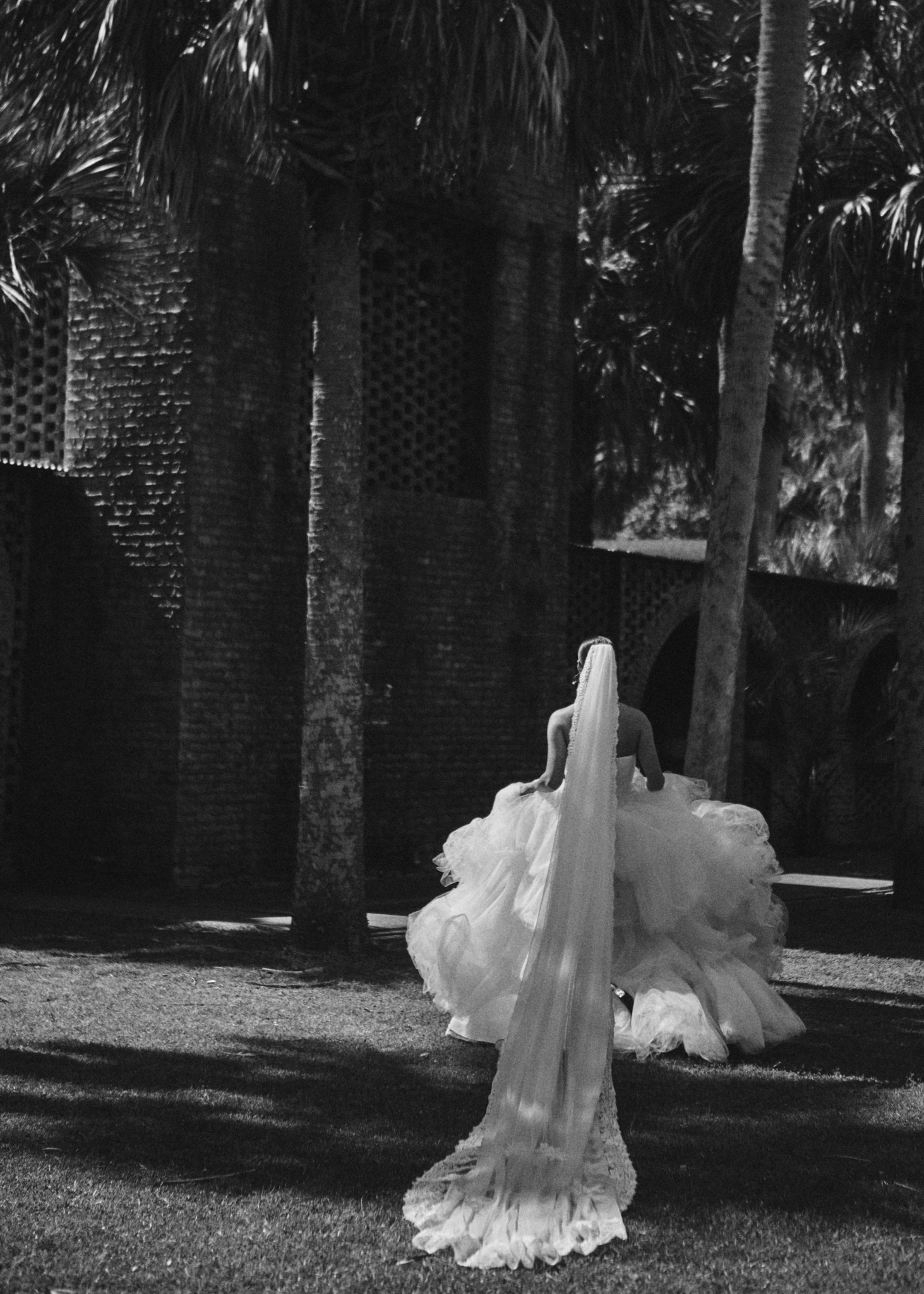 A person in a flowing dress stands outdoors among trees and shadows.
