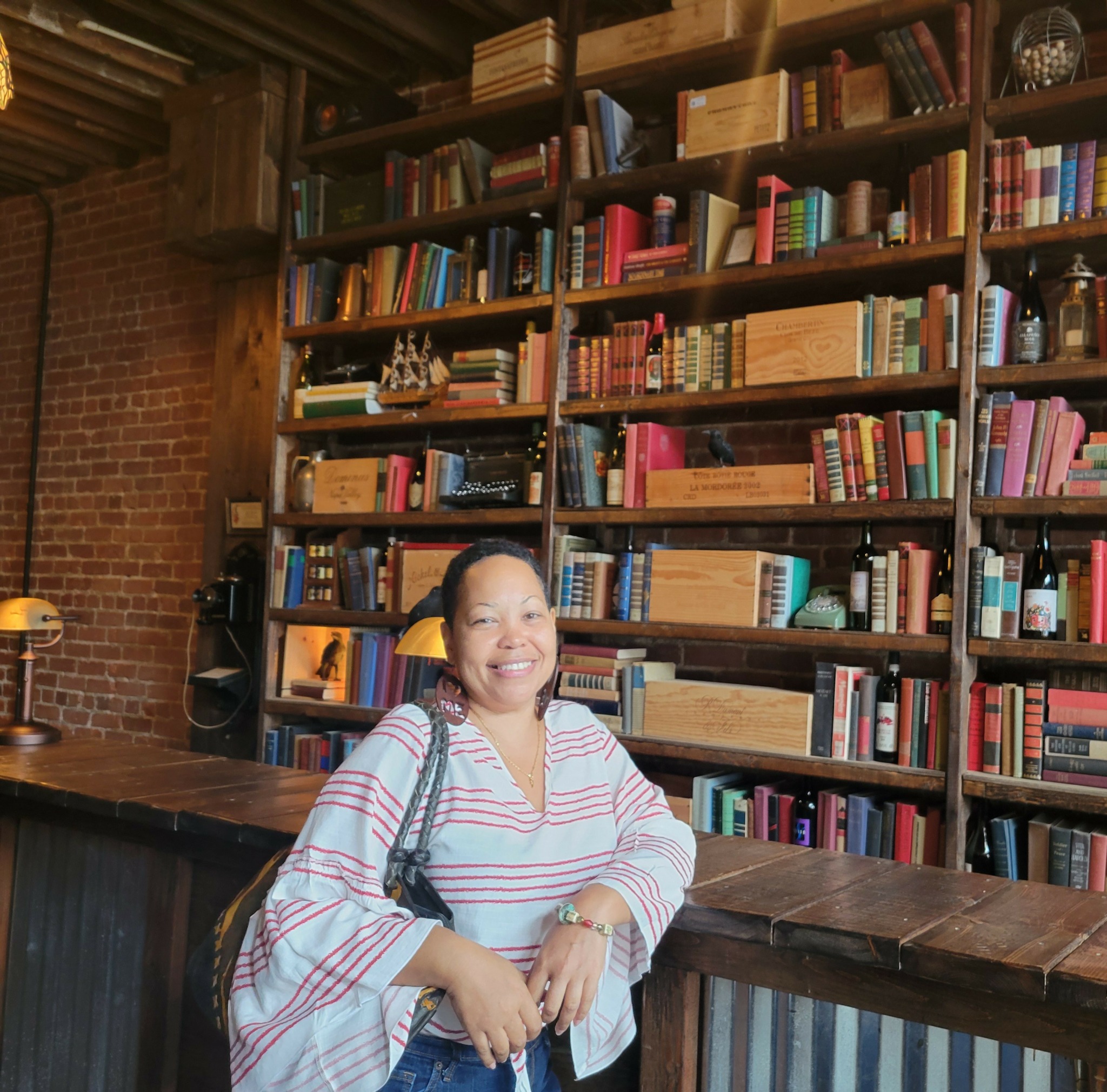 Smiling woman standing in front of a large bookshelf filled with books in a cozy library setting.