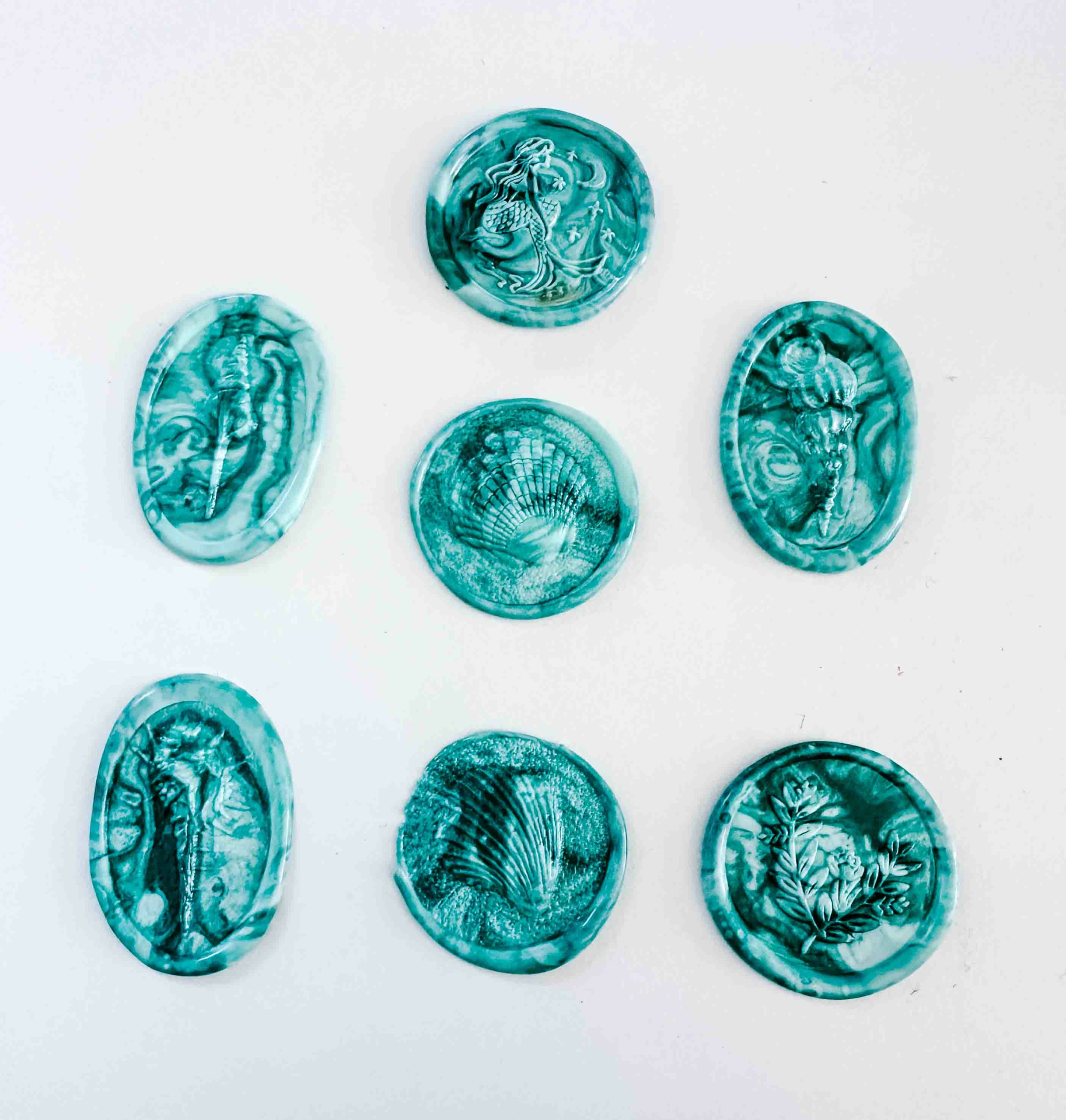 Seven round, teal-colored objects with intricate patterns on a white background.