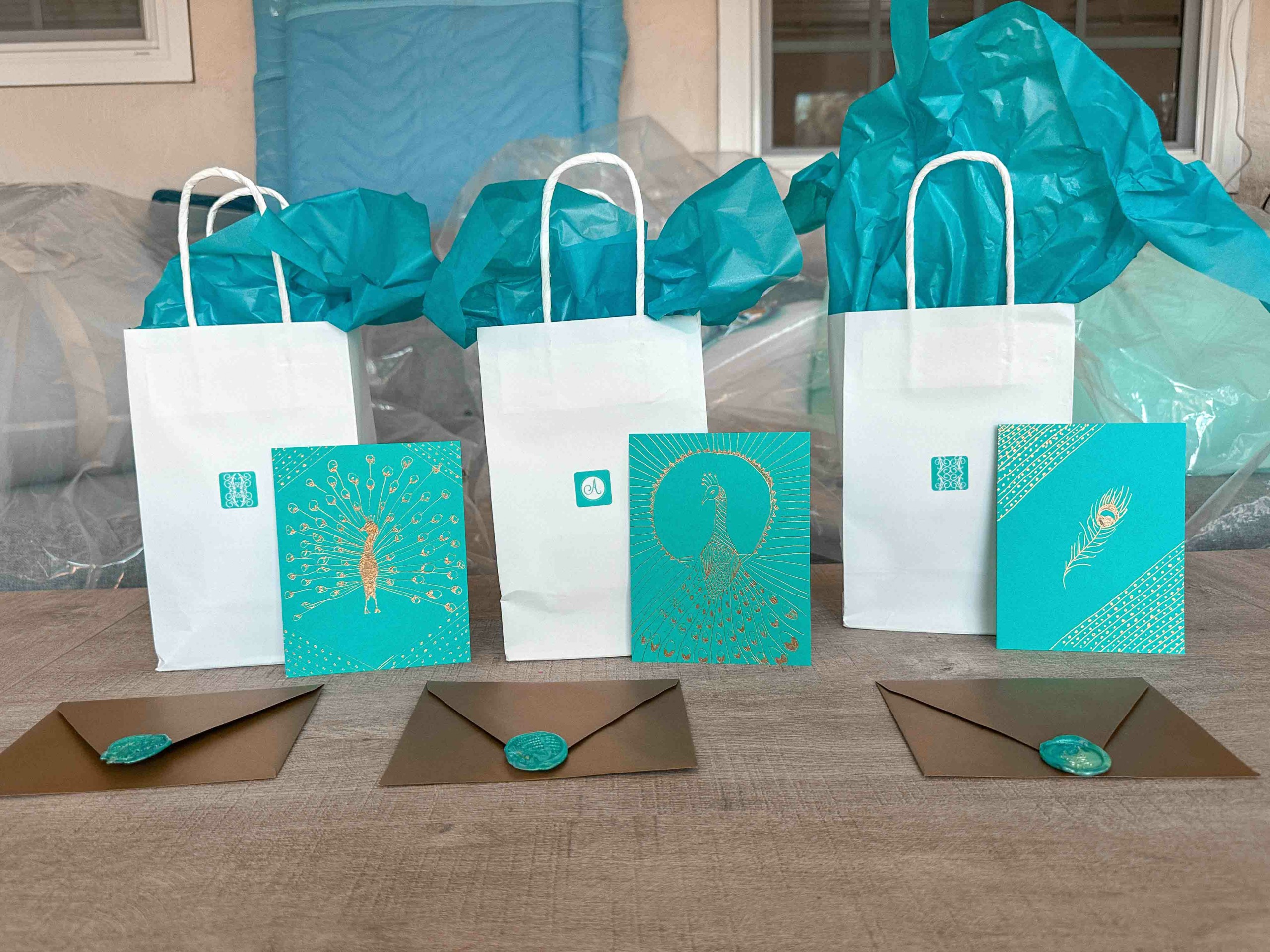 Four white gift bags with blue tissue paper and three cards with fish, headphones, and a feather design, on a table.