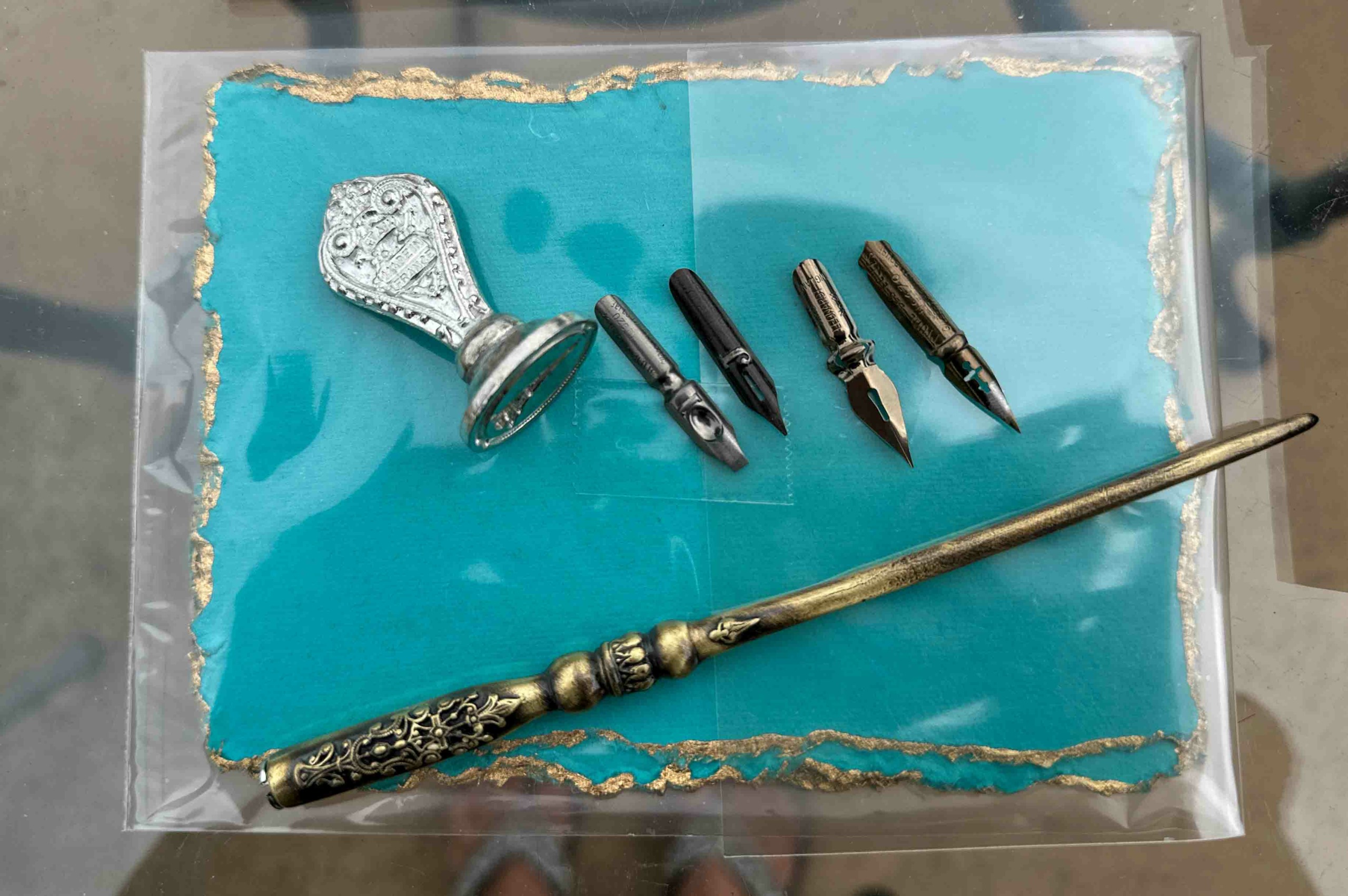 Decorative dagger with a long, ornate gold handle and a pointed blade, alongside four small metallic objects and a silver bell.