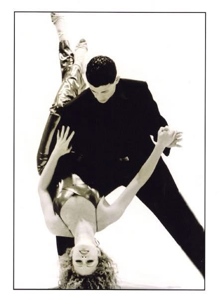 A man in a black suit dances with a woman in a dress, both in a dance pose, black and white image.