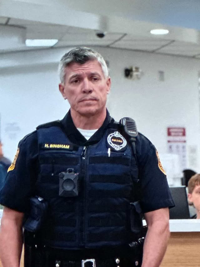 Police officer in uniform standing indoors with a serious expression.