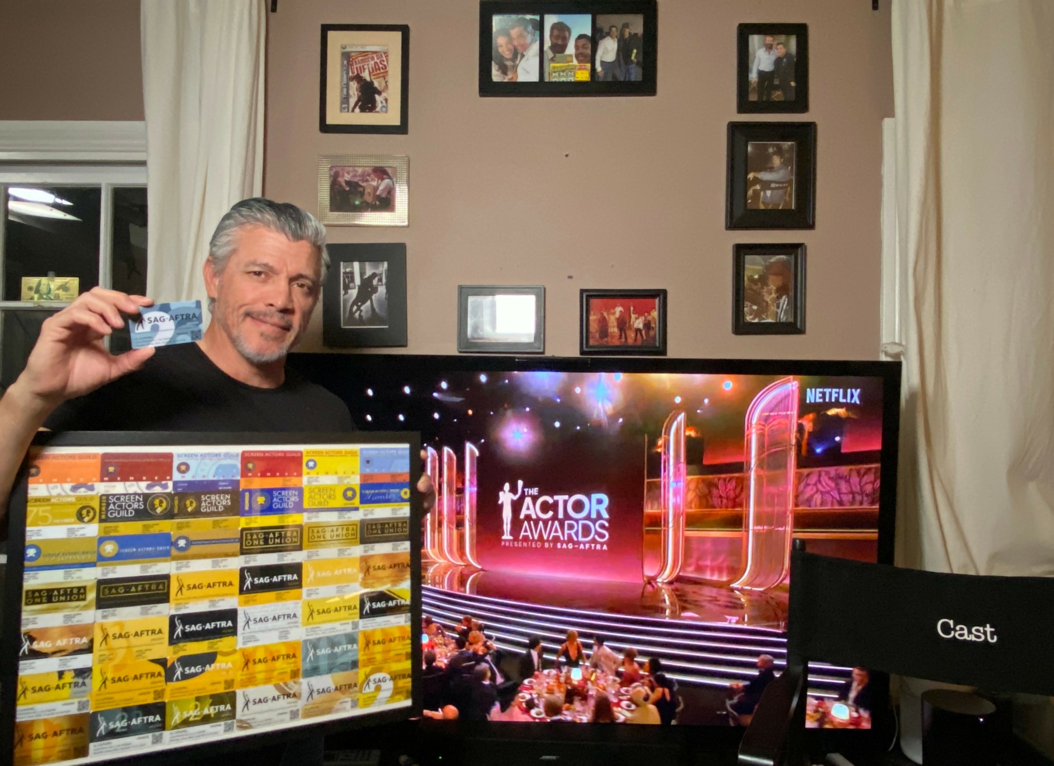 Man holding an award trophy in front of a large screen displaying 'Actor Awards' and a stage scene.
