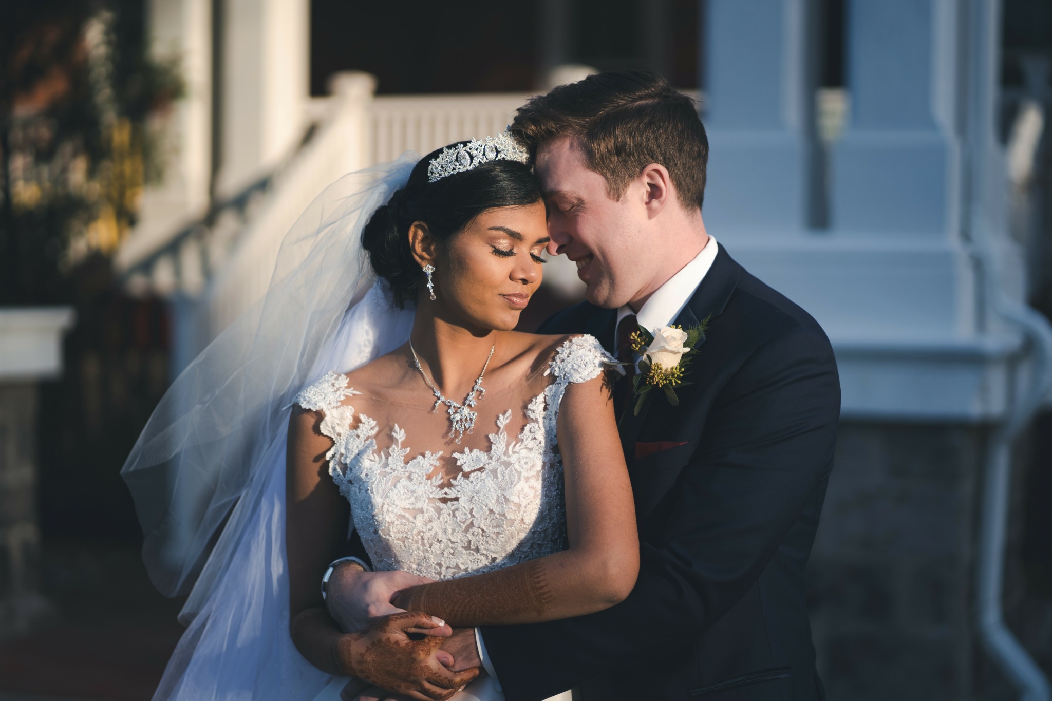 Bride and groom embrace outdoors, bride in wedding dress with veil, groom in suit, close together, tender moment.
