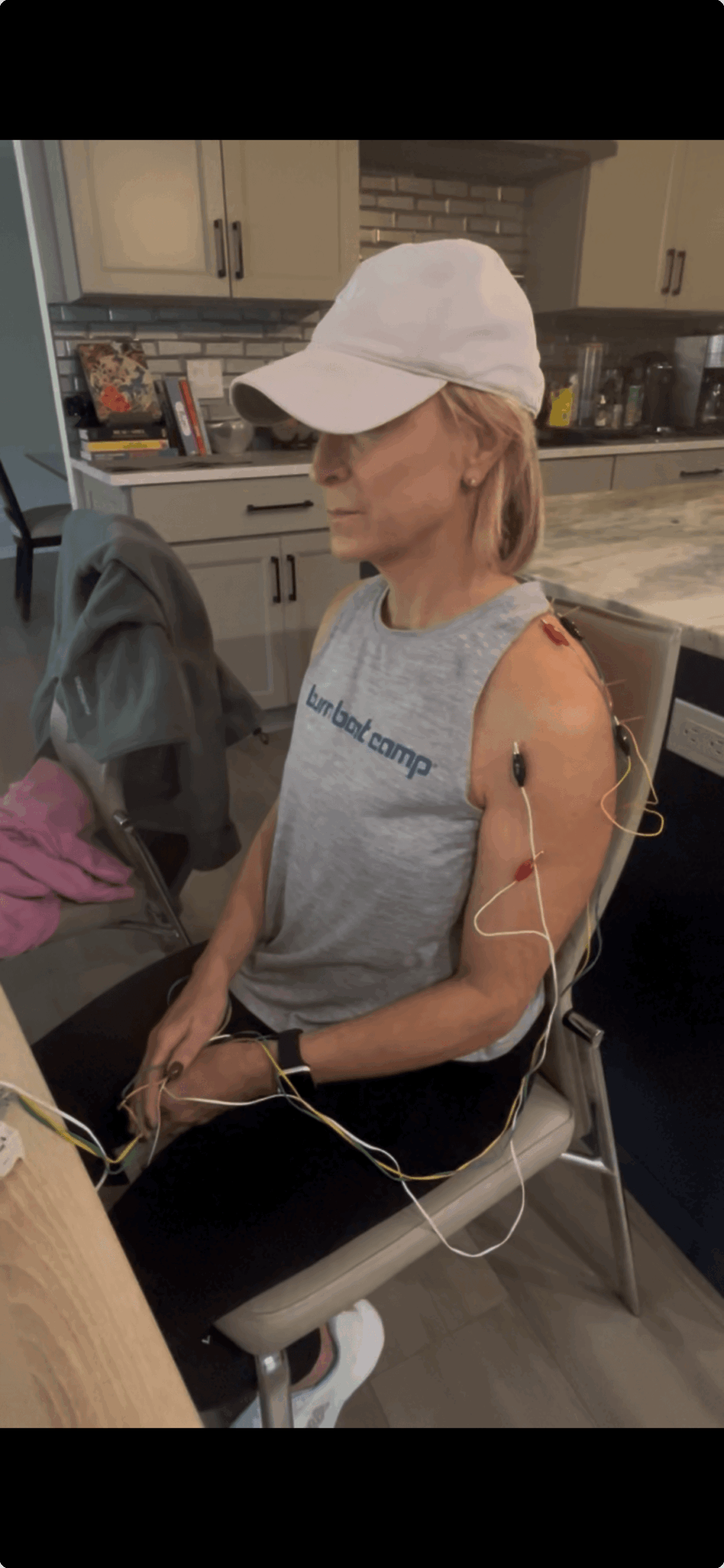 Woman sitting in a medical setting with IV line in her arm, wearing a white cap and sleeveless shirt.