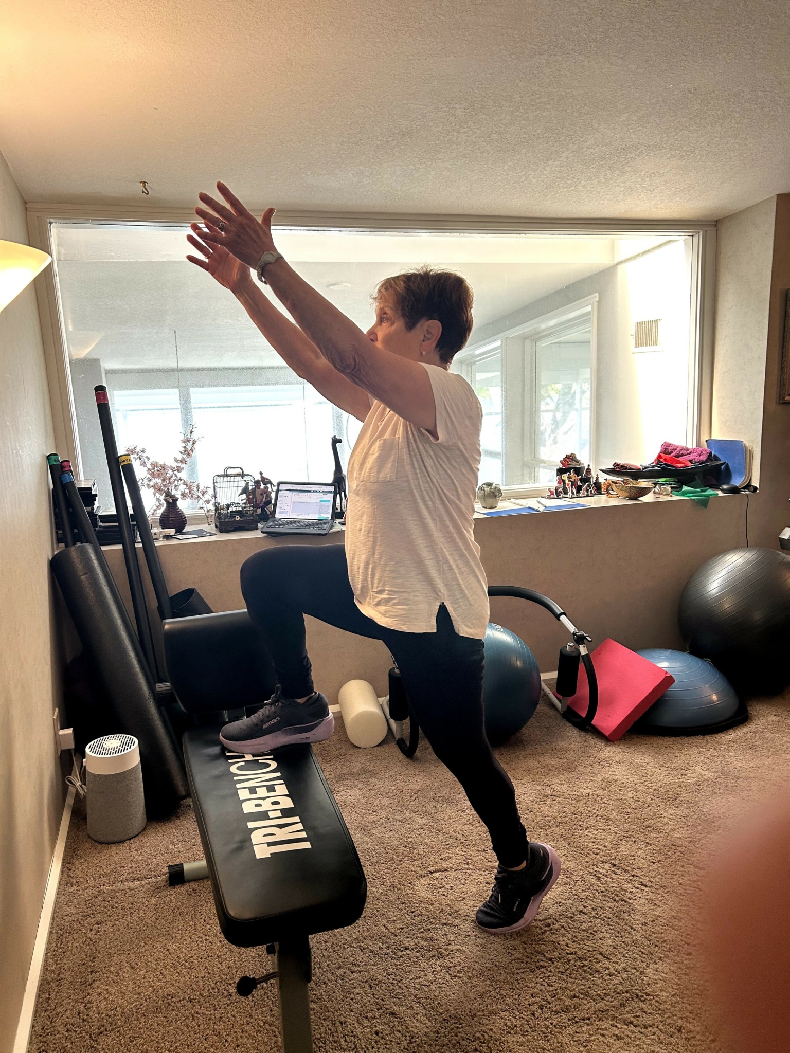 Woman performing a balance exercise on a workout bench in a home gym, with fitness equipment around.