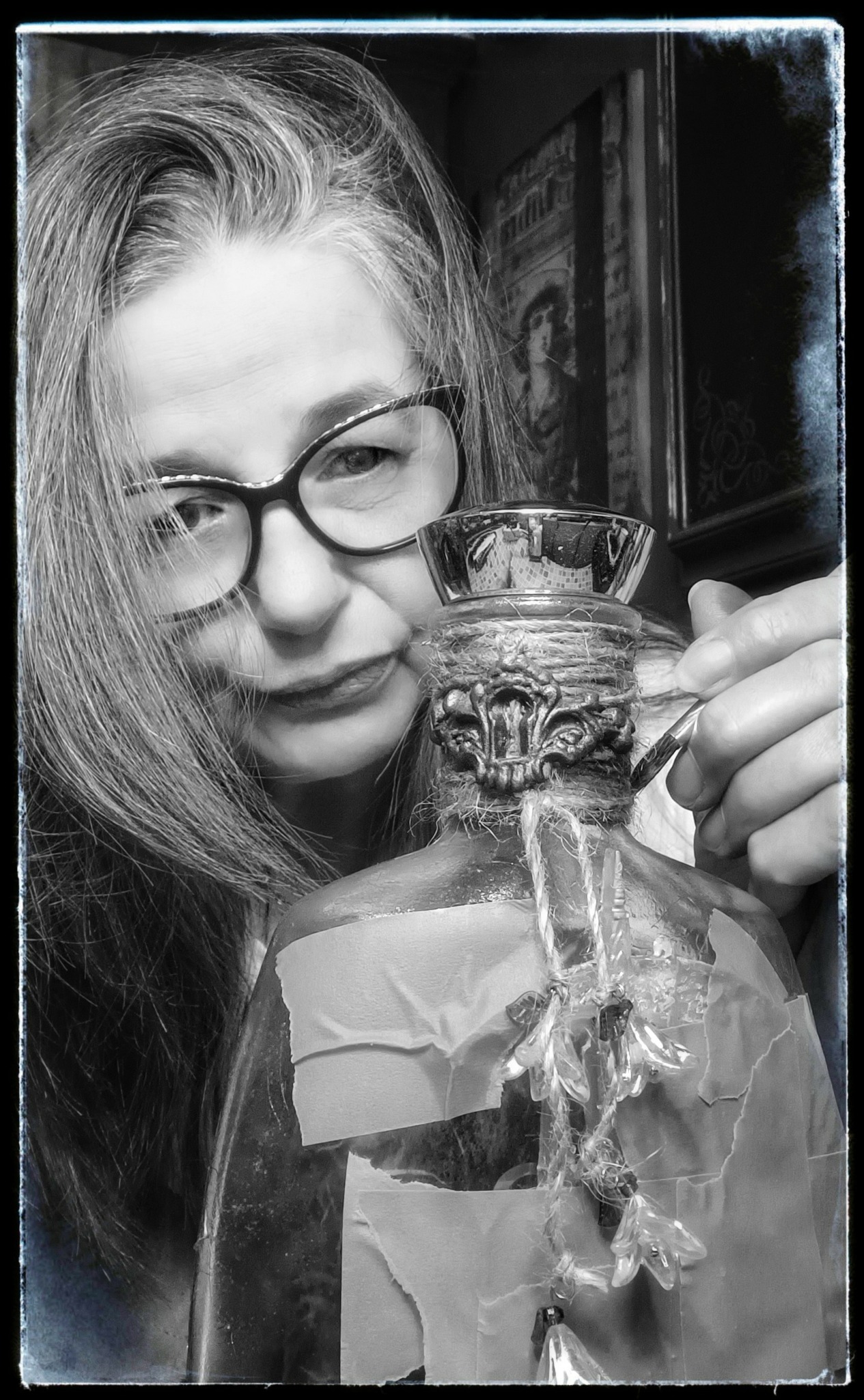 Woman with glasses holding a glass pitcher with a lion face design, looking at it closely.