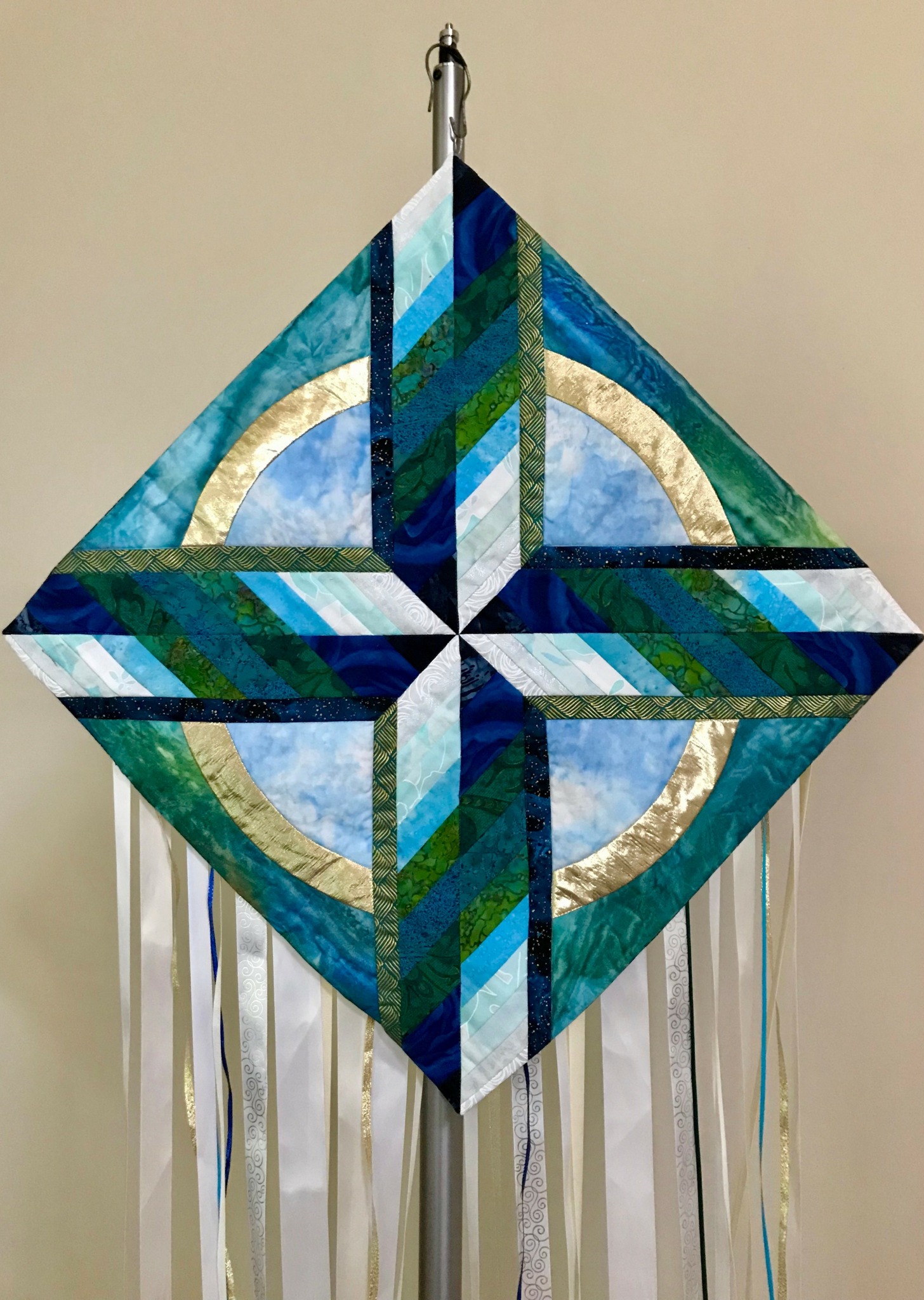Colorful diamond-shaped kite with geometric patterns and ribbons hanging from the bottom, set against a plain background.