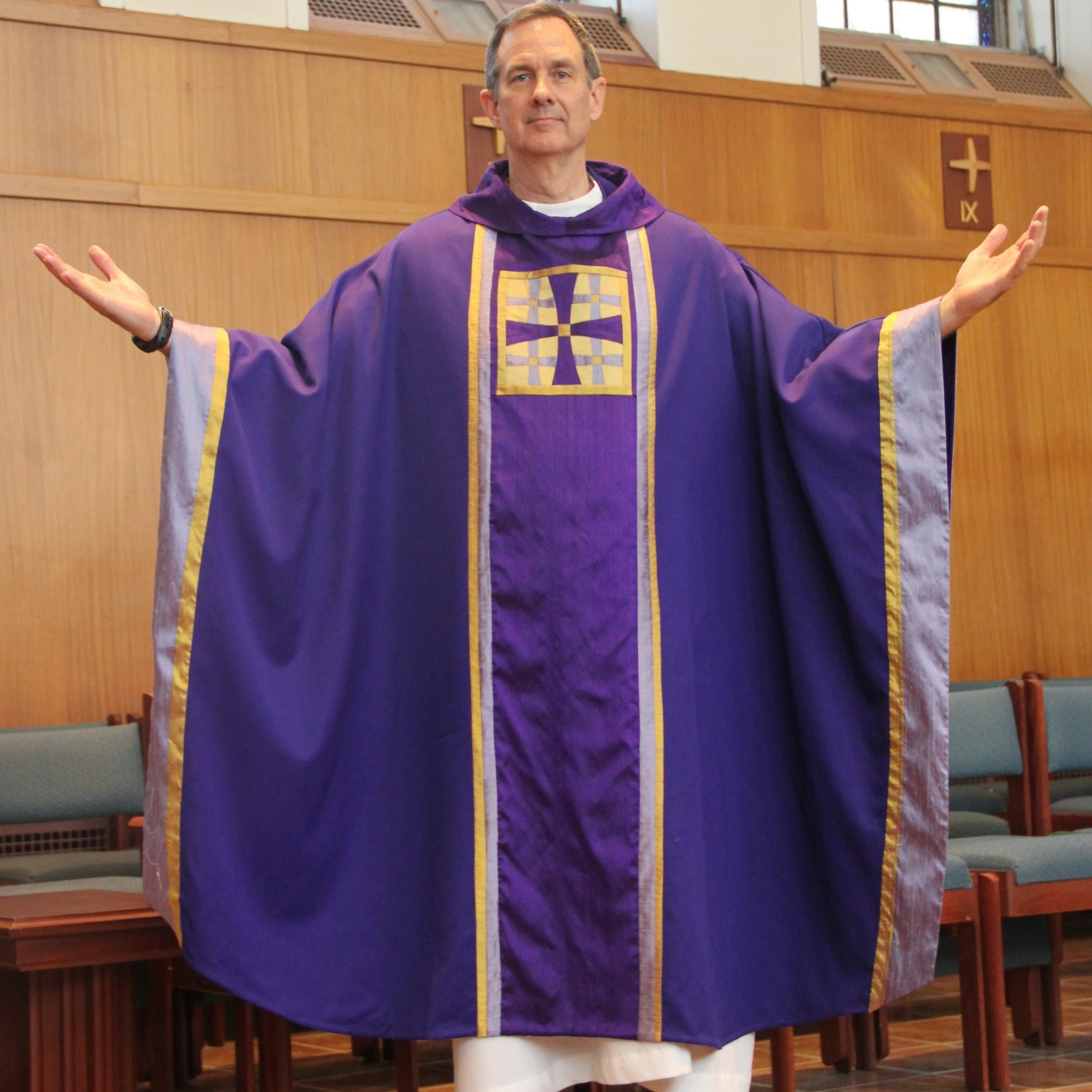 Man in purple religious robe with gold trim, arms outstretched, standing in church interior.