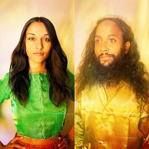Two people with long hair, one with straight hair and the other with curly hair, wearing colorful clothing.