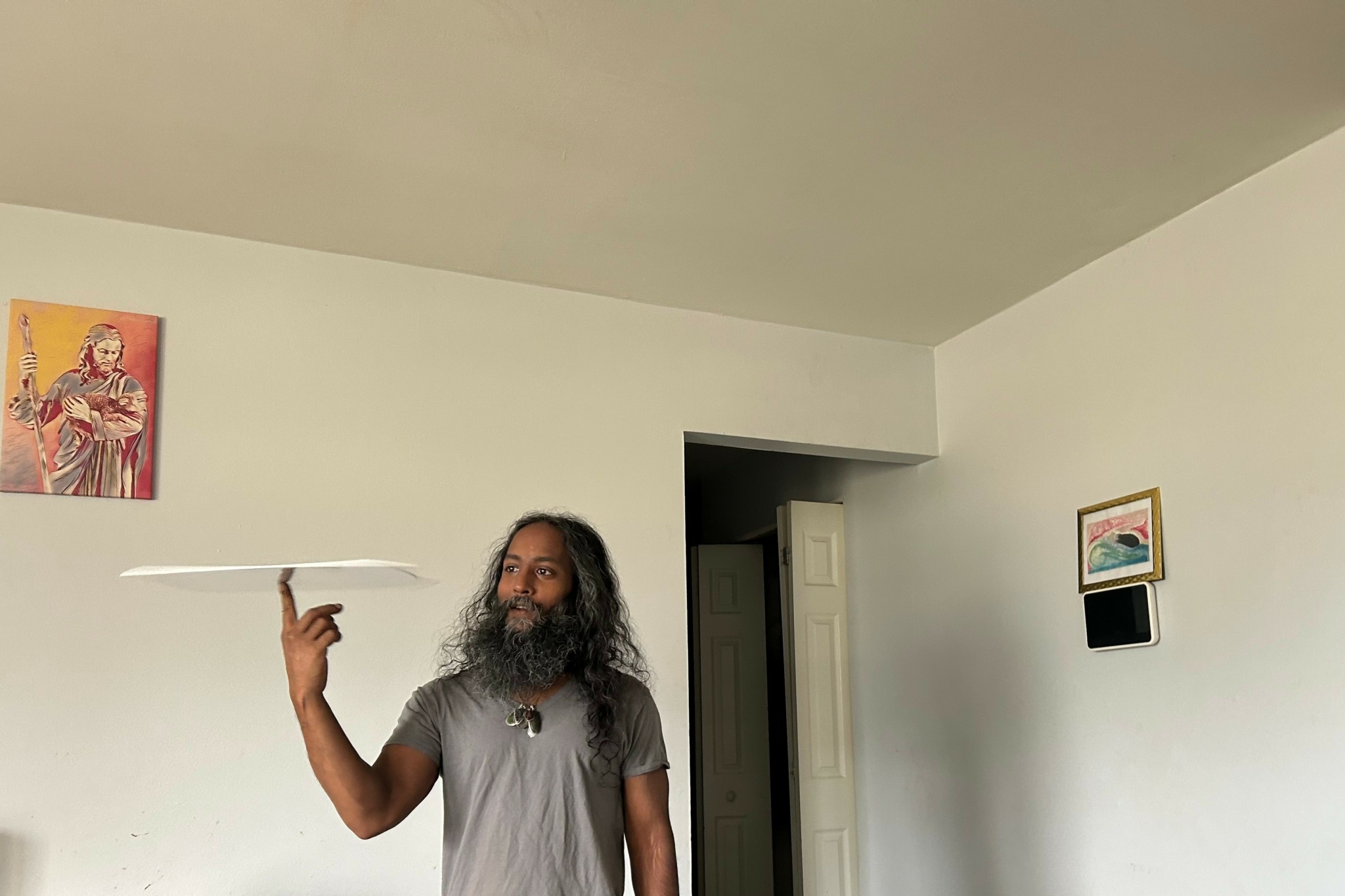 Man with long hair and beard holding a plate in a room with white walls.