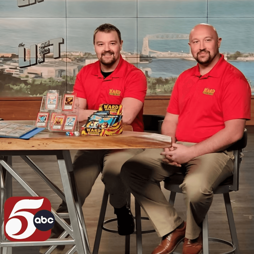 Two men in red shirts sitting at a table with board games, in front of a window with a bridge view.