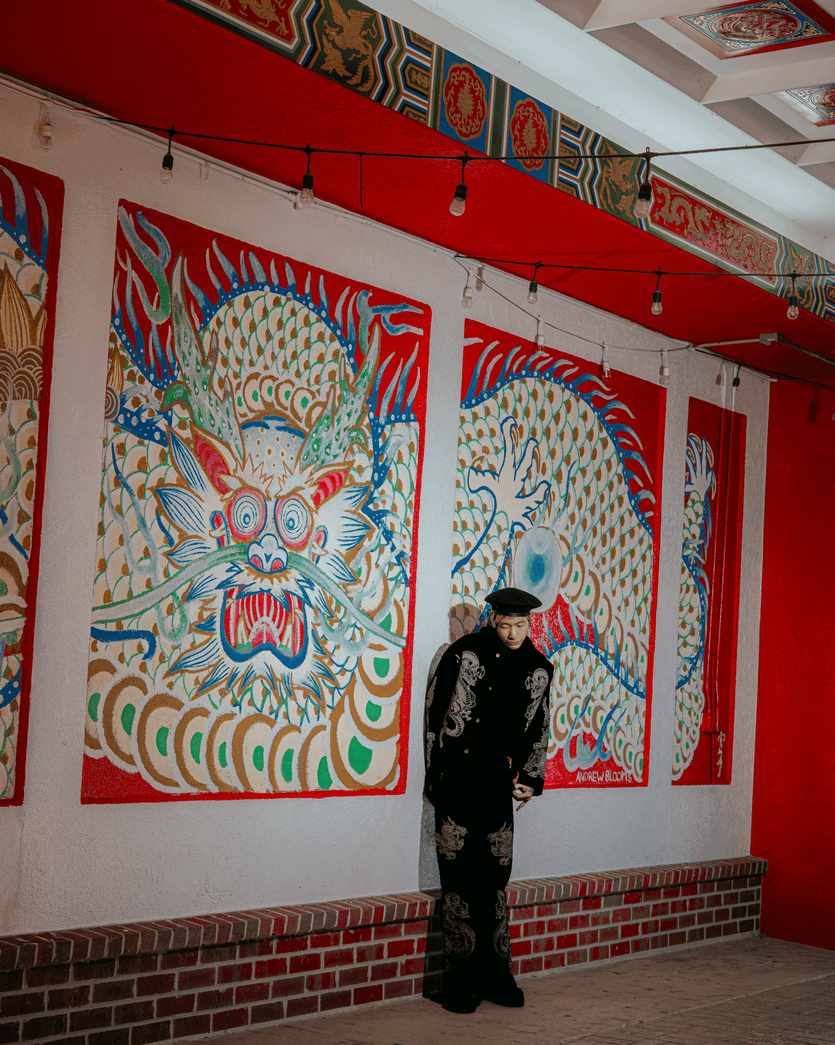 Person standing in front of colorful dragon and lion artwork on white wall, with red ceiling and brick baseboard.