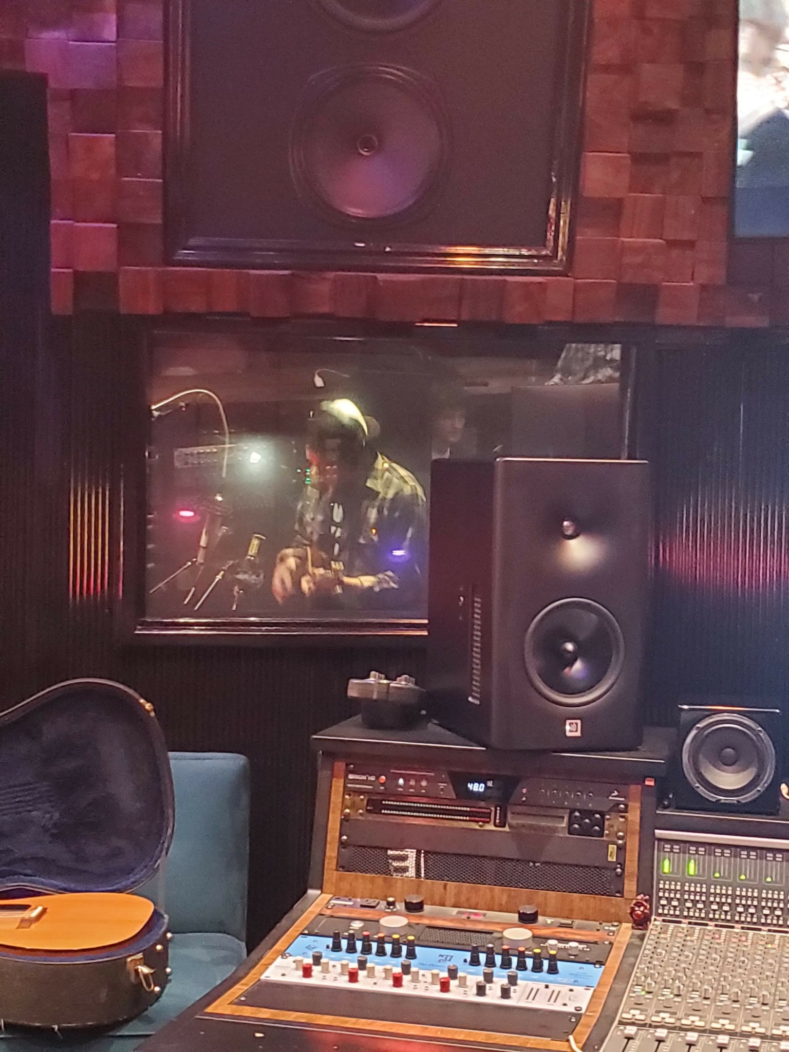 Music studio with speakers, mixing console, and a mirror reflecting a person in the room.