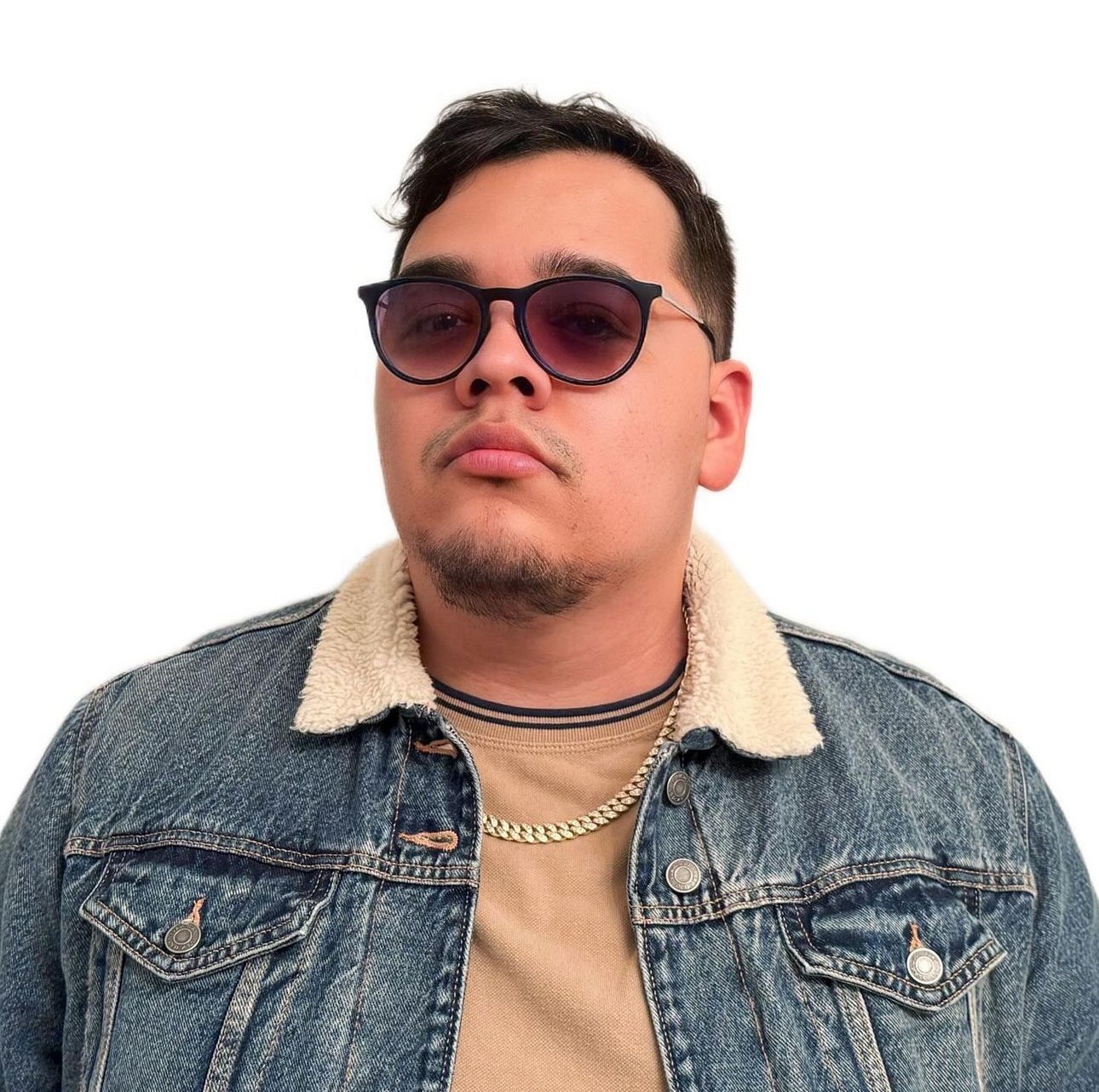 Young man wearing sunglasses, denim jacket, and a chain necklace, looking serious against a white background.