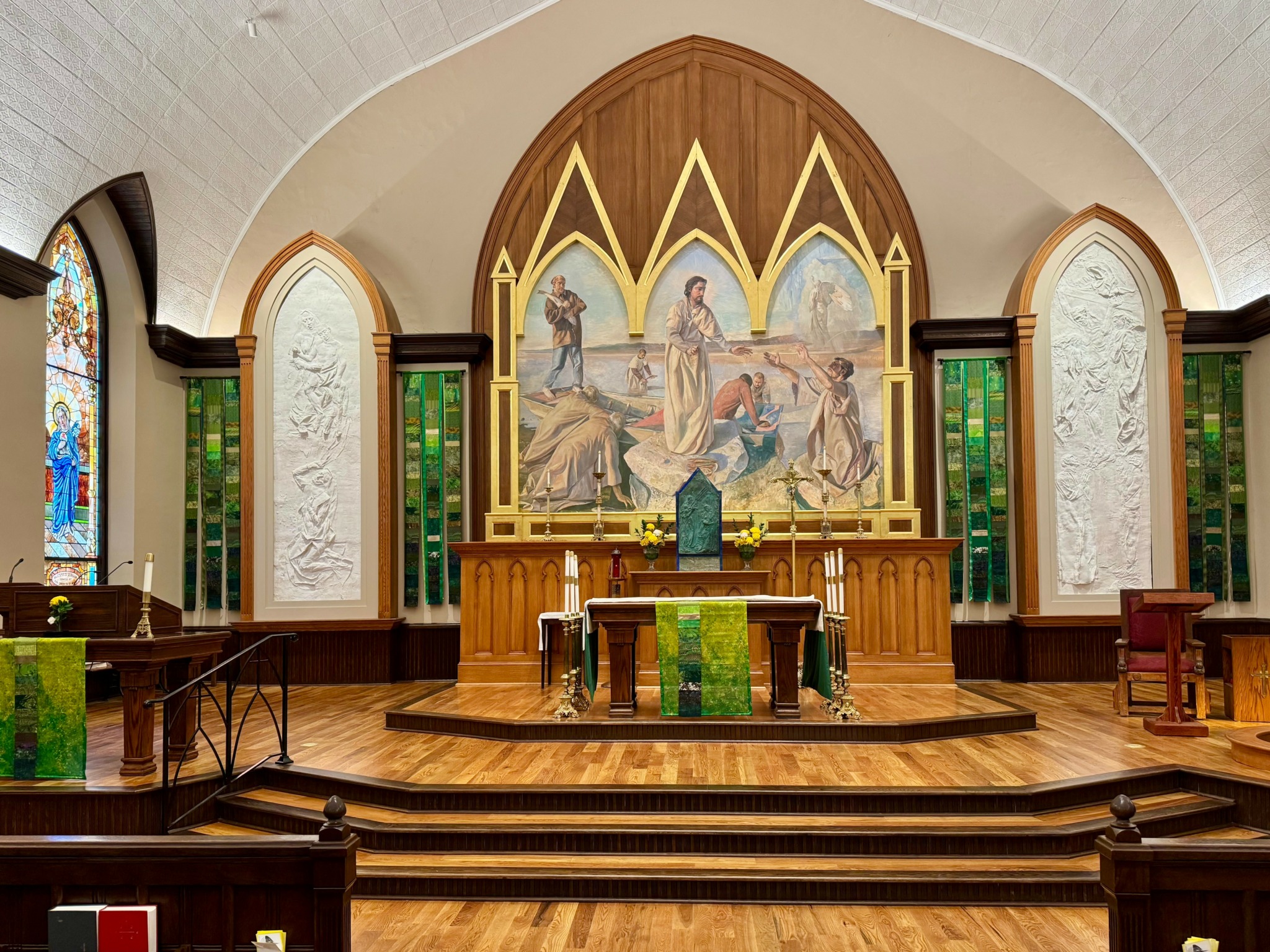 Interior of a church altar with a large central painting, wooden altar table, and stained glass windows on sides.