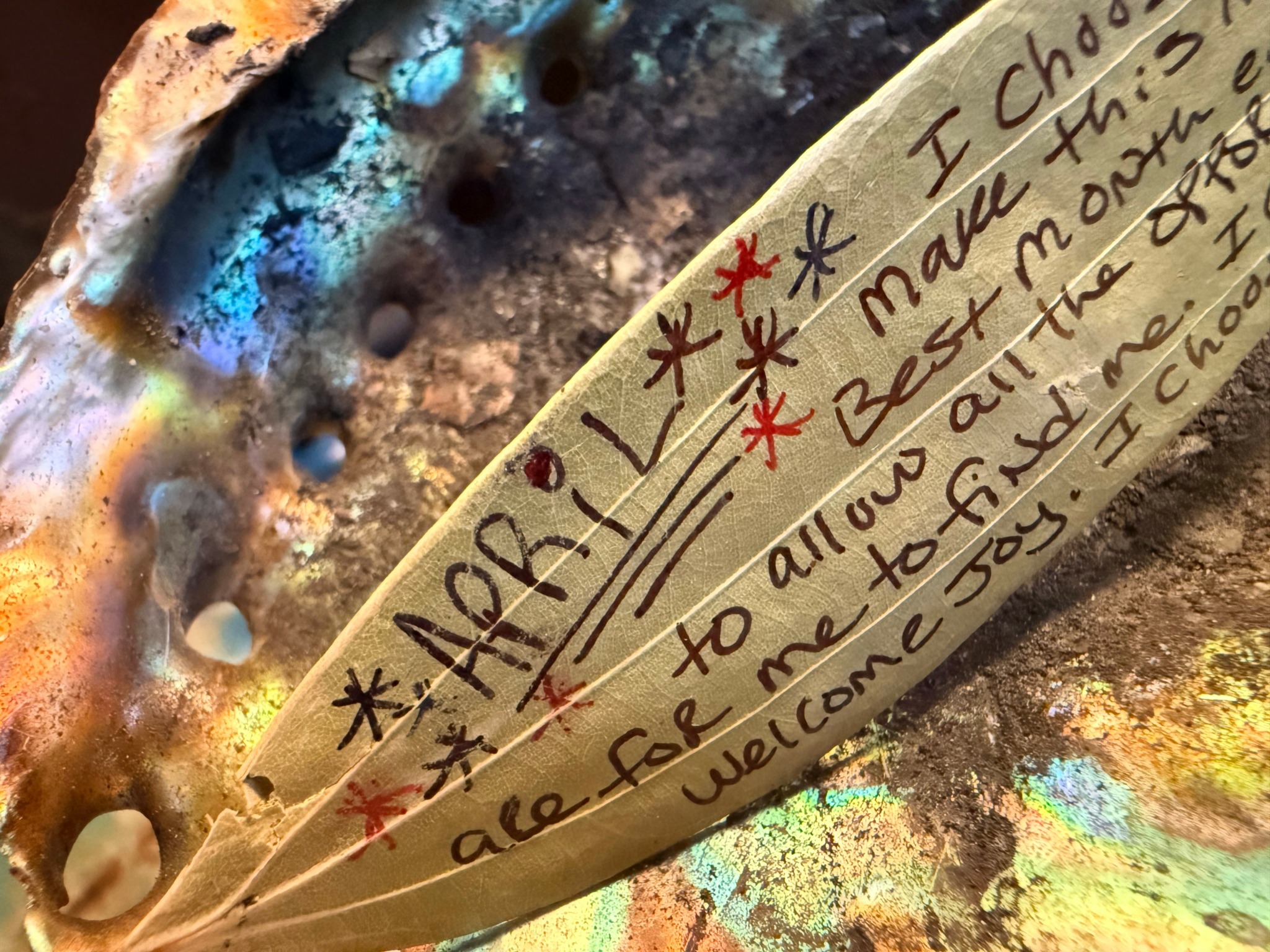Close-up of a handwritten note on a leaf with colorful, textured background, and red star symbols around the text.