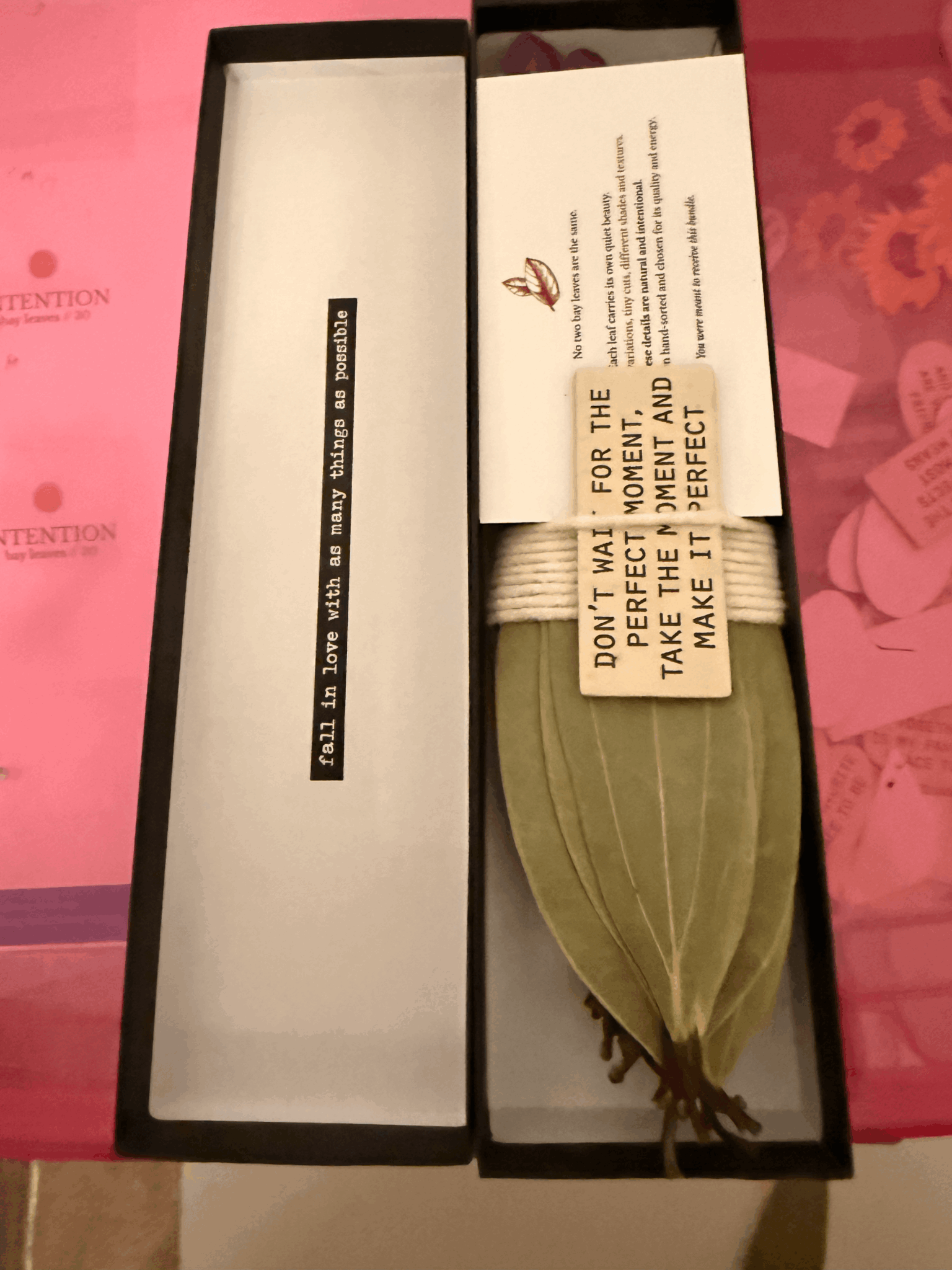 Open box with a leaf-shaped item and paper notes inside, pink background with floral pattern.
