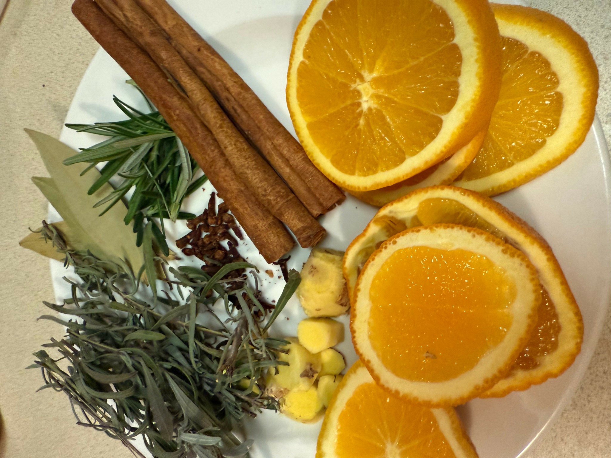 Slices of orange, cinnamon sticks, and herbs on a white plate.