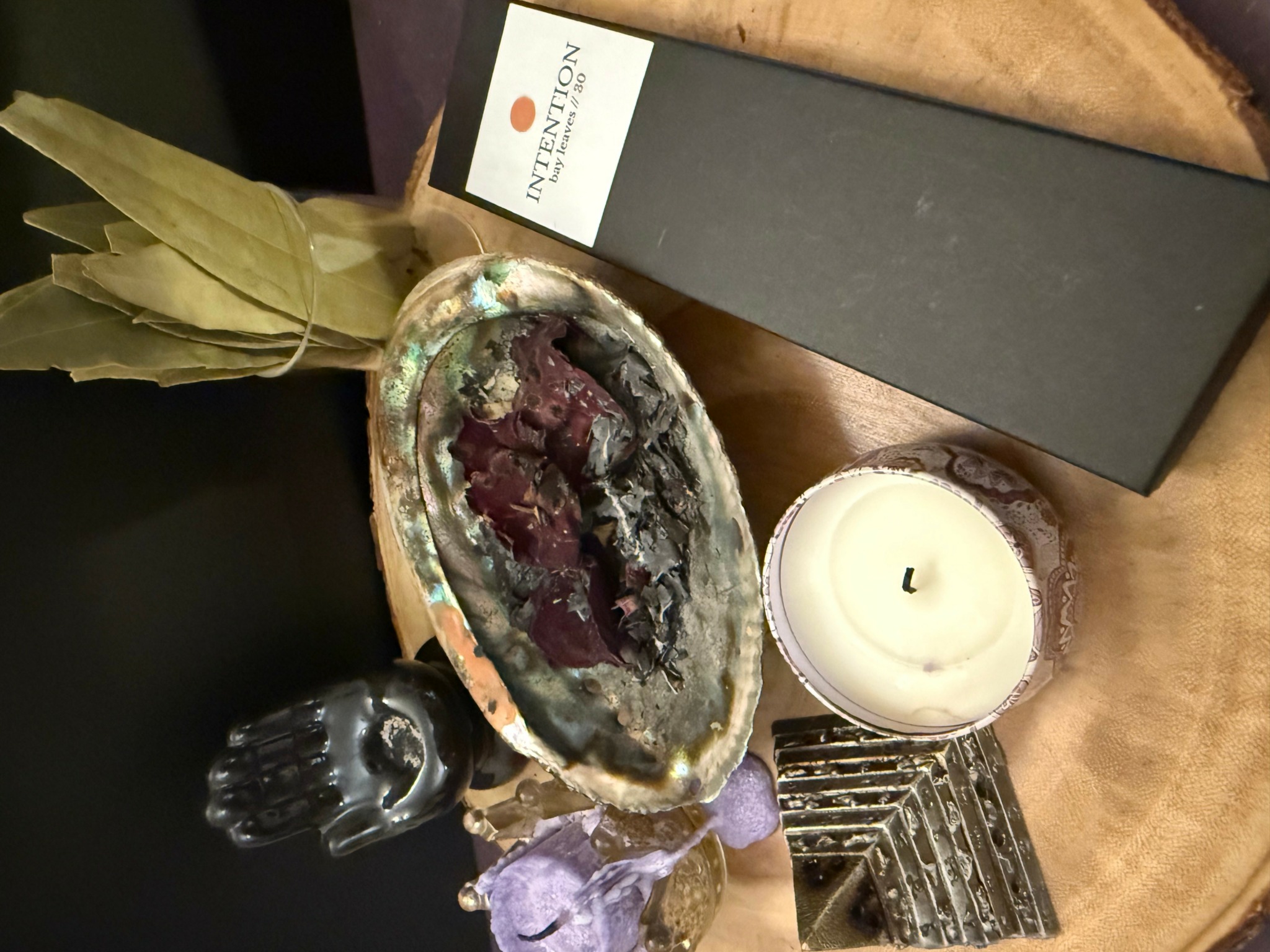 Black box, candle, purple crystal, and decorative object on wooden surface with dried leaves.