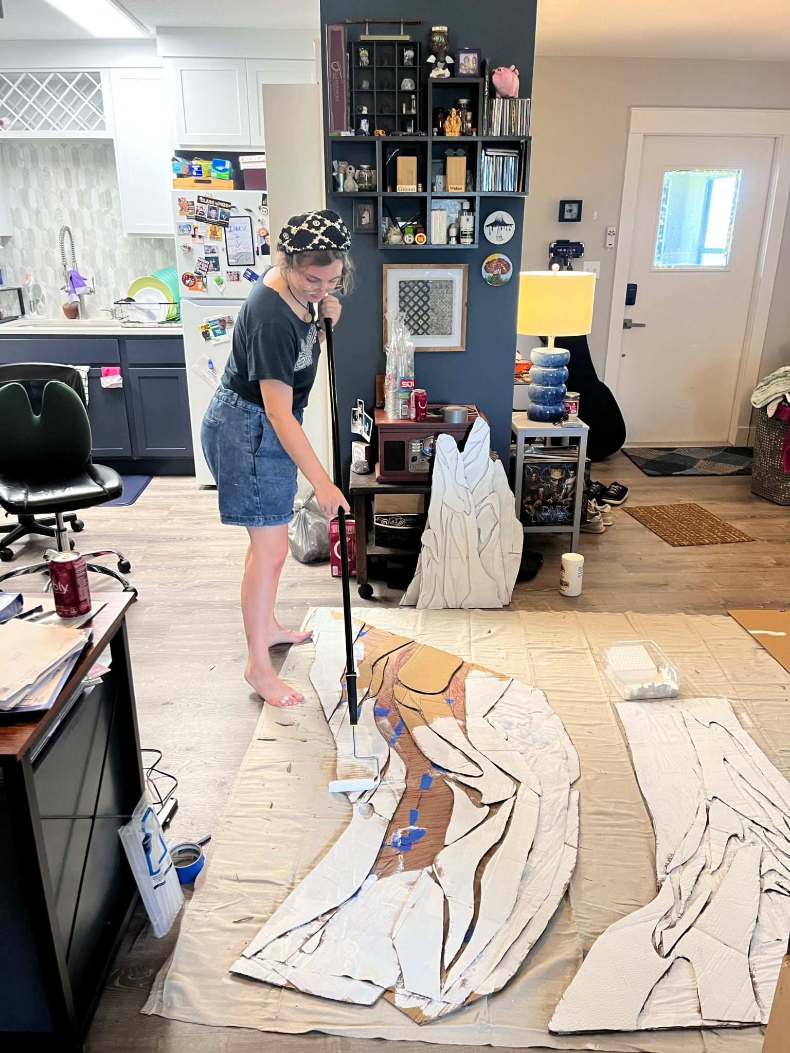 Person standing on a rug in a room, working on a large, patterned fabric or paper piece on the floor.