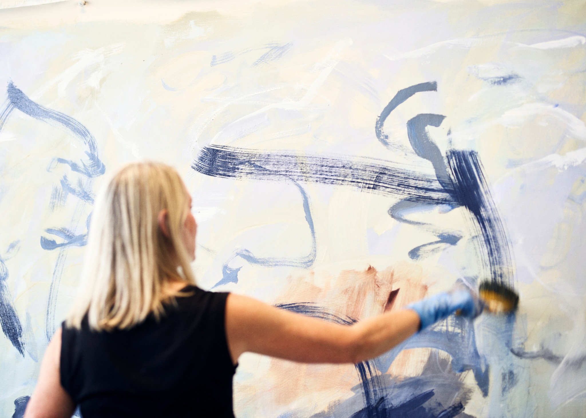 Person painting on a large canvas with broad brushstrokes, facing away from the camera.