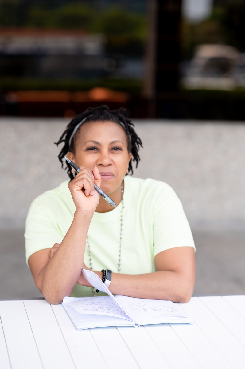 Woman with headphones and a pen, sitting at a table with a notebook outdoors.