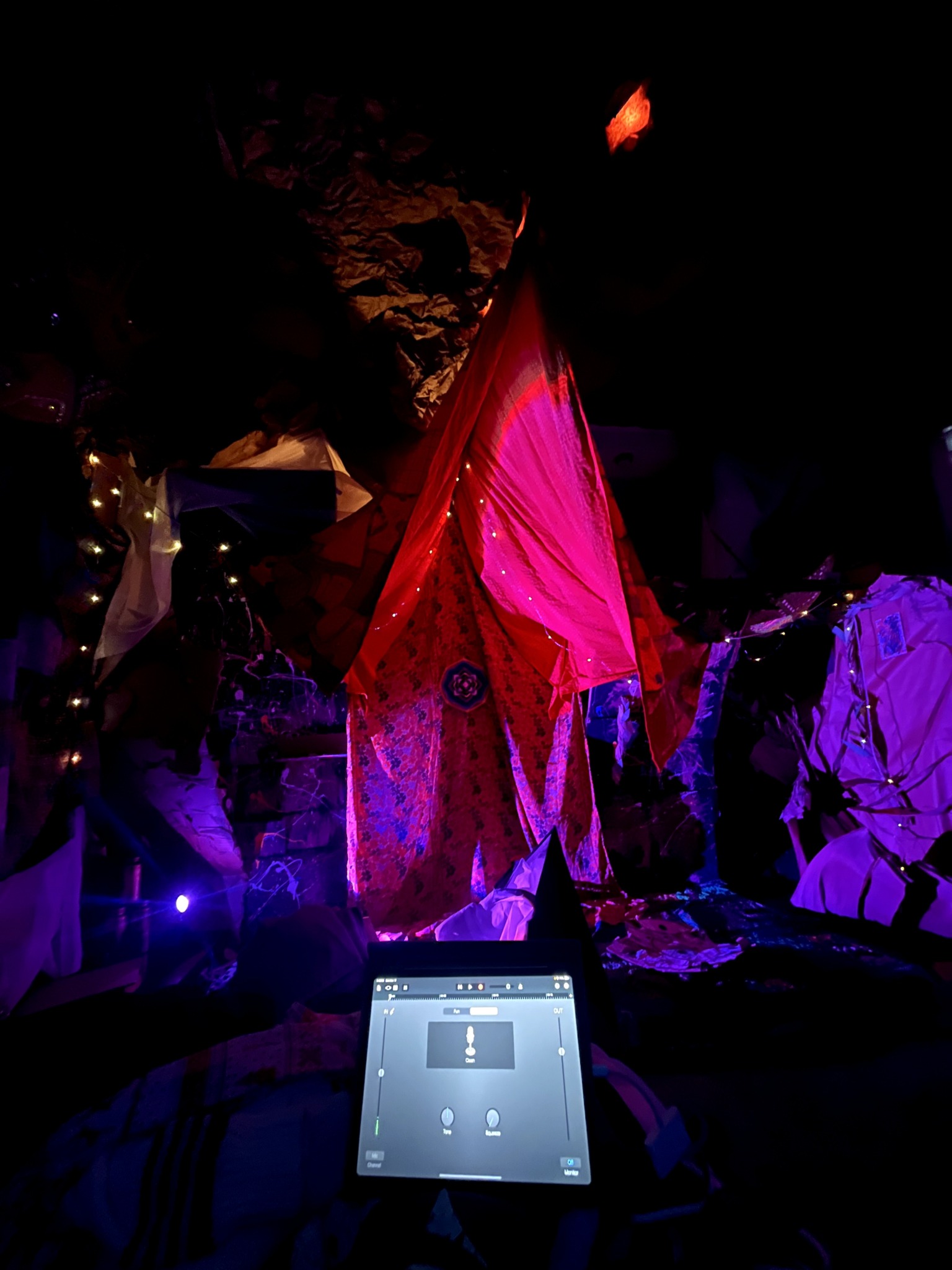 Colorful fabric draped over a structure illuminated with purple and pink lights, with a tablet in the foreground.