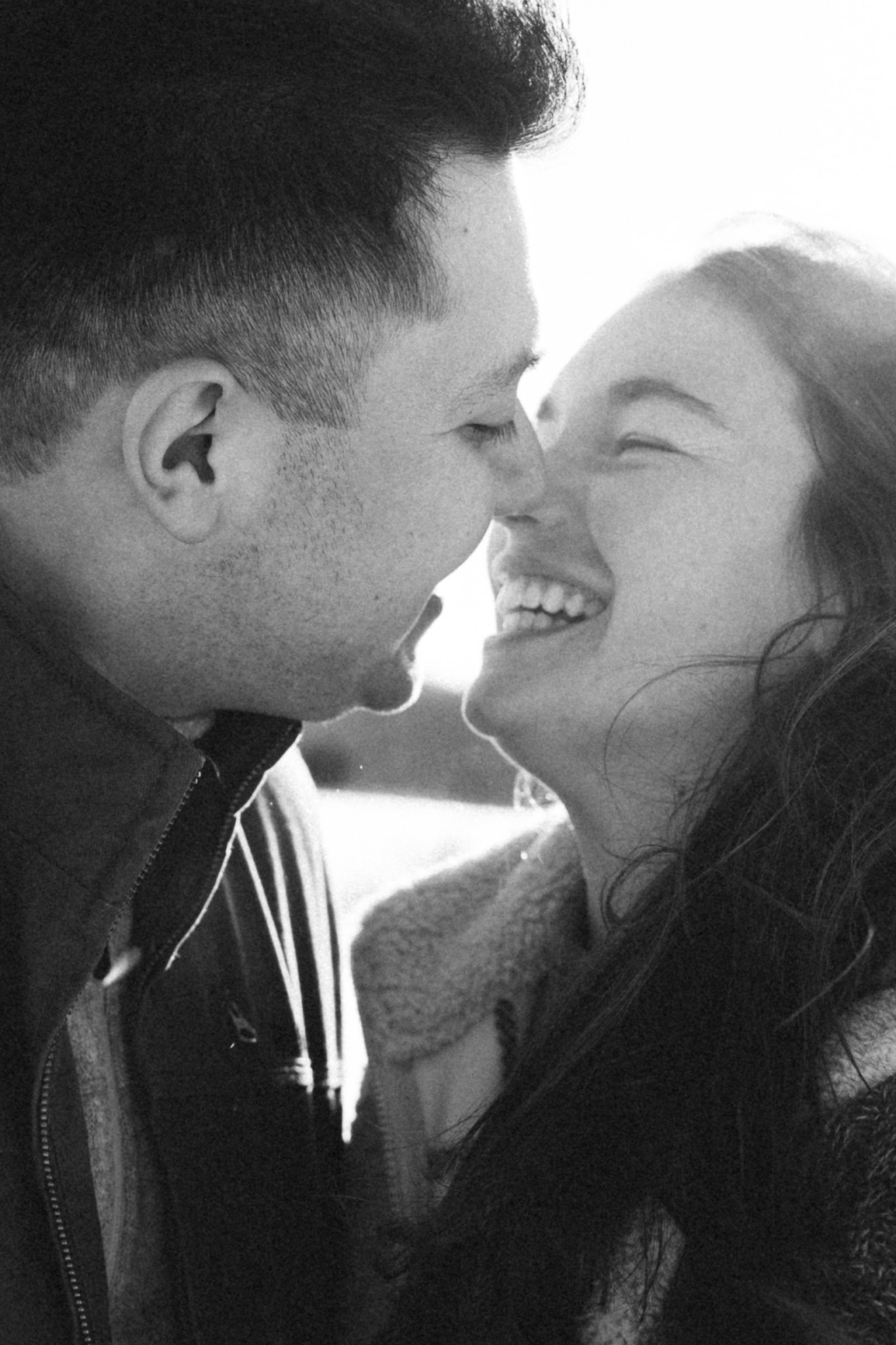 Two people smiling close together, faces nearly touching, in black and white.