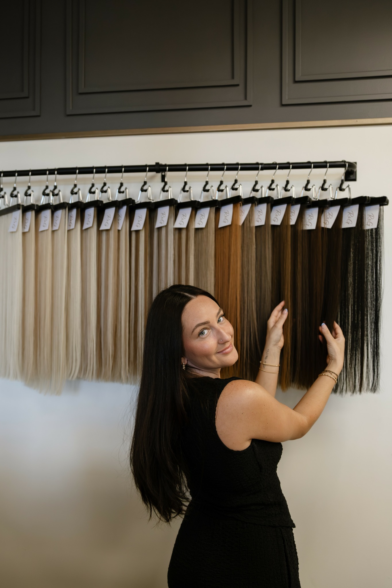Woman with long dark hair smiling and touching fabric samples hanging on a wall.