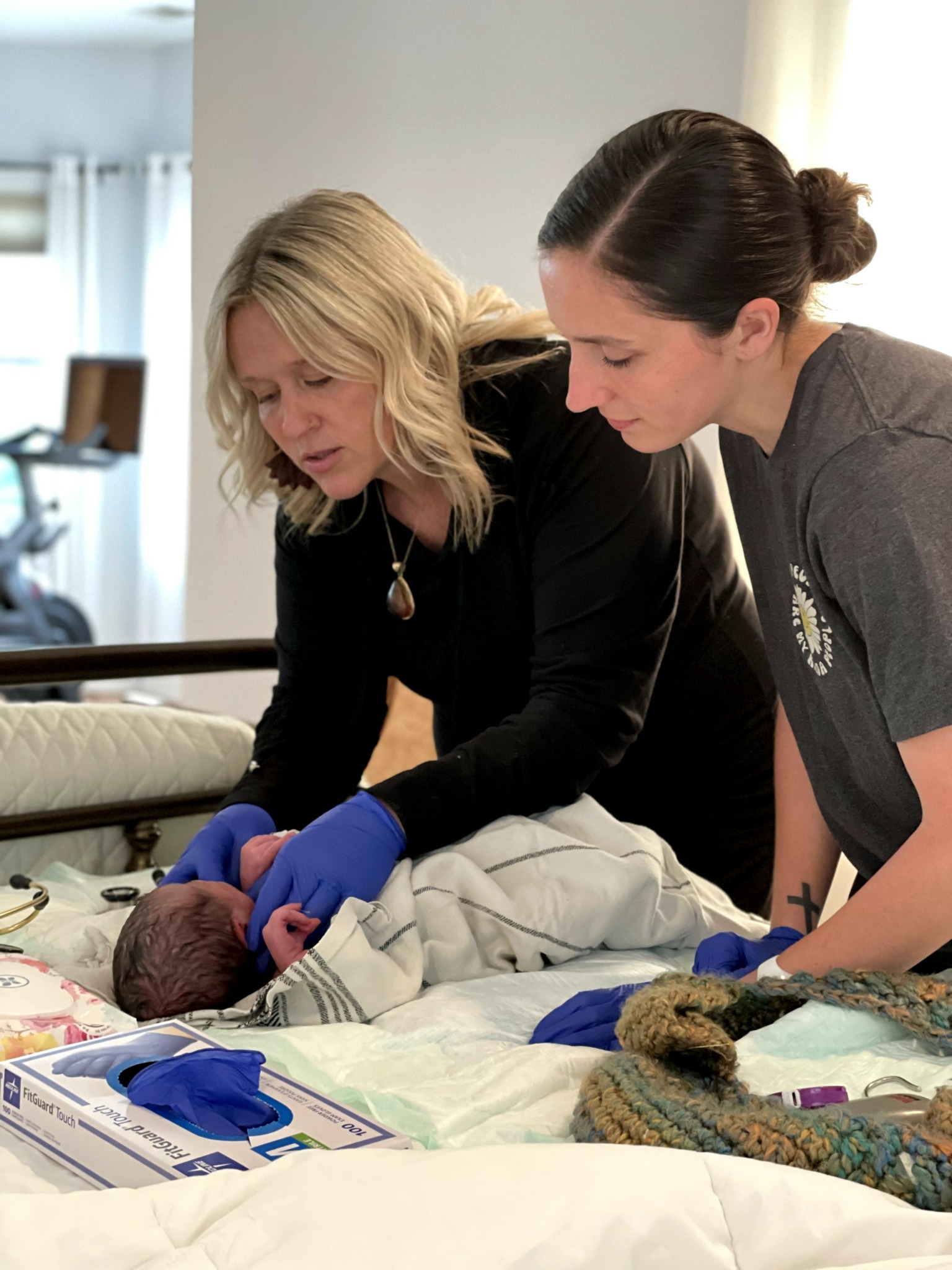 Two women attend to a newborn baby on a hospital bed, with medical supplies nearby.