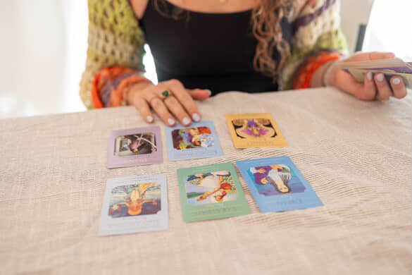 Person sitting at table with seven colorful cards laid out, holding a smartphone in one hand.