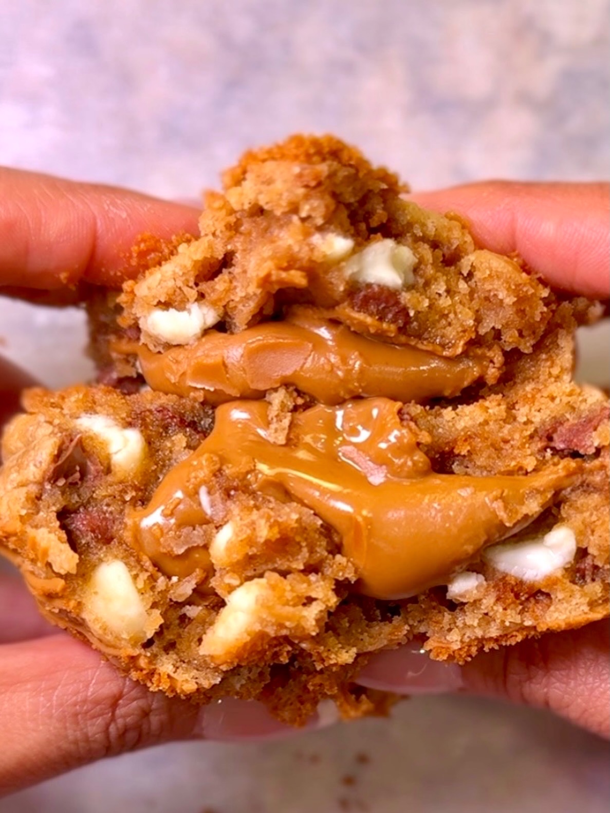 Close-up of a hand holding a broken fried chicken piece with caramel and marshmallow filling inside.