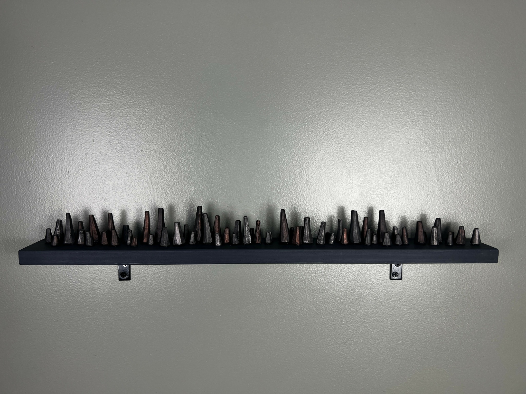 Black shelf with numerous small objects on it, mounted on a plain wall.