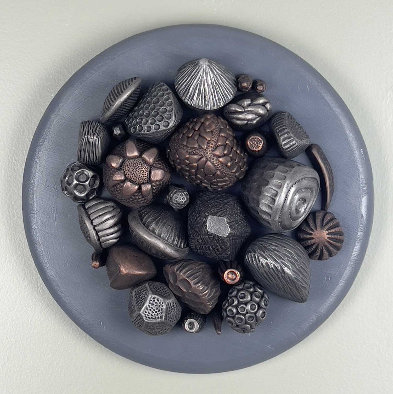 Round gray plate filled with various black and gray decorative beads and objects, some with textured surfaces.