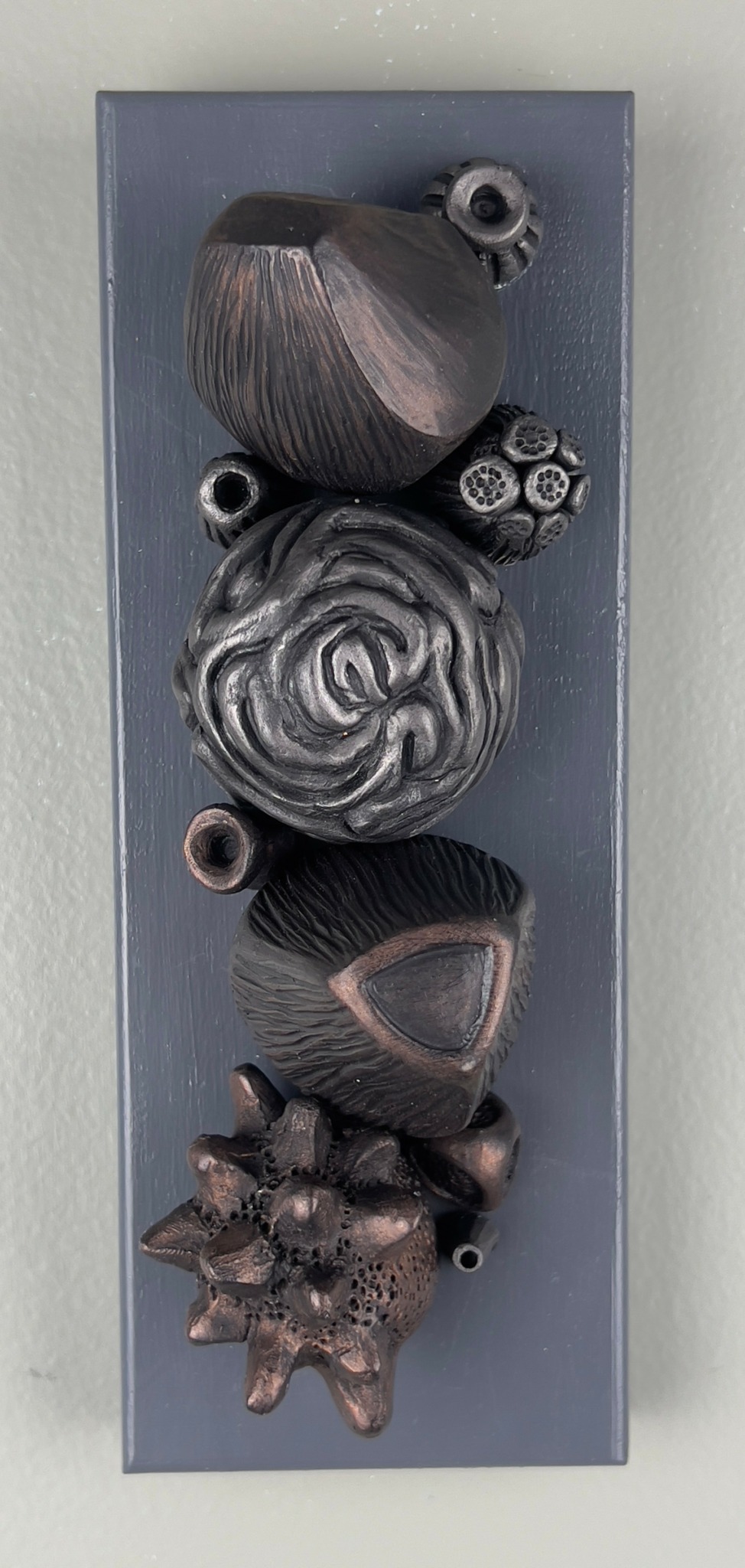 Five metallic, textured, abstract sculptures arranged vertically on a rectangular base.