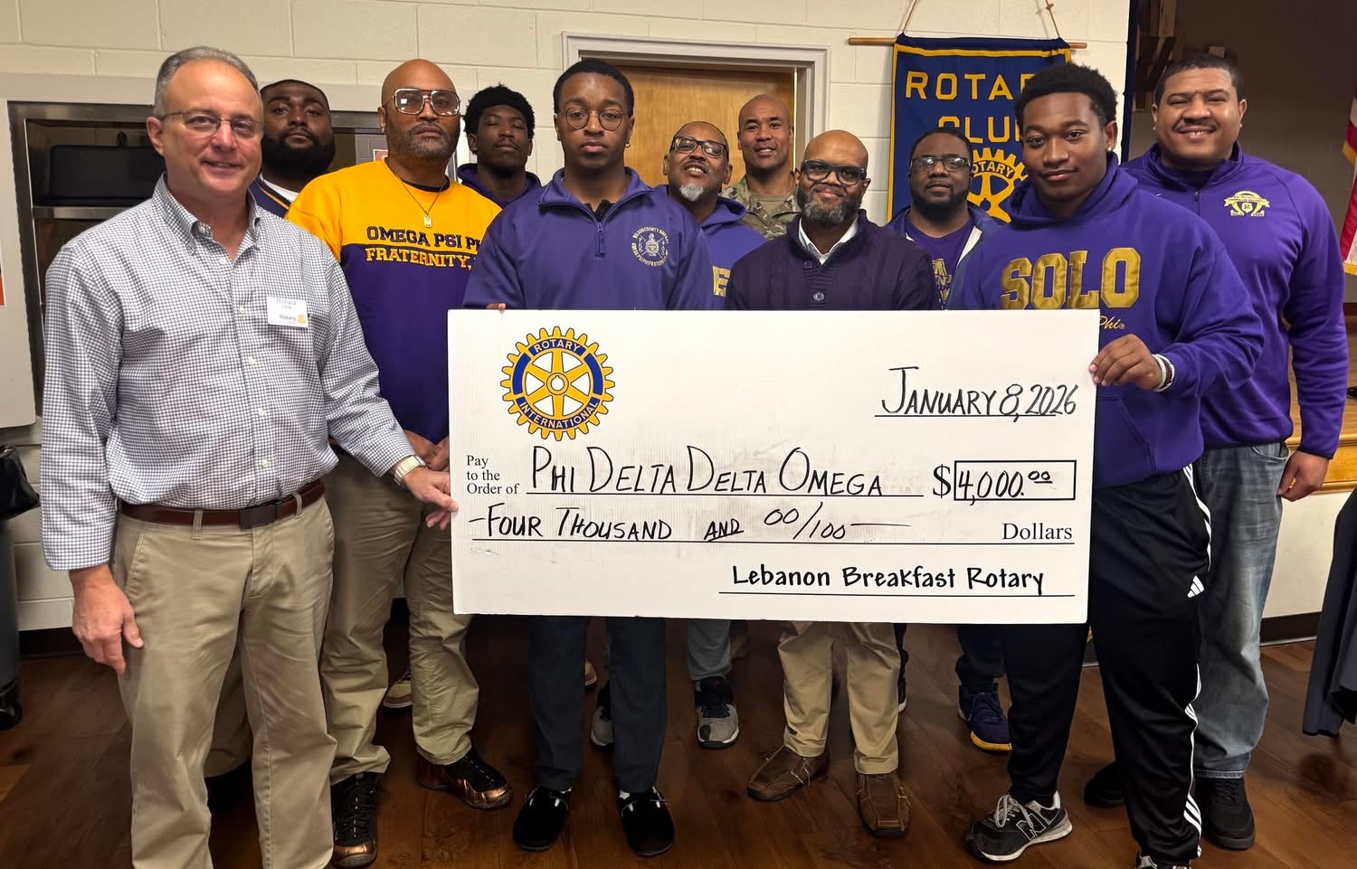 Group of people holding a large check for four thousand dollars, with Rotary banners in the background.