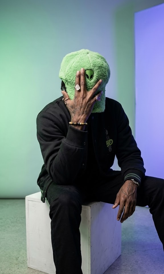 Person sitting on a white block holding a green textured ball in front of their face.
