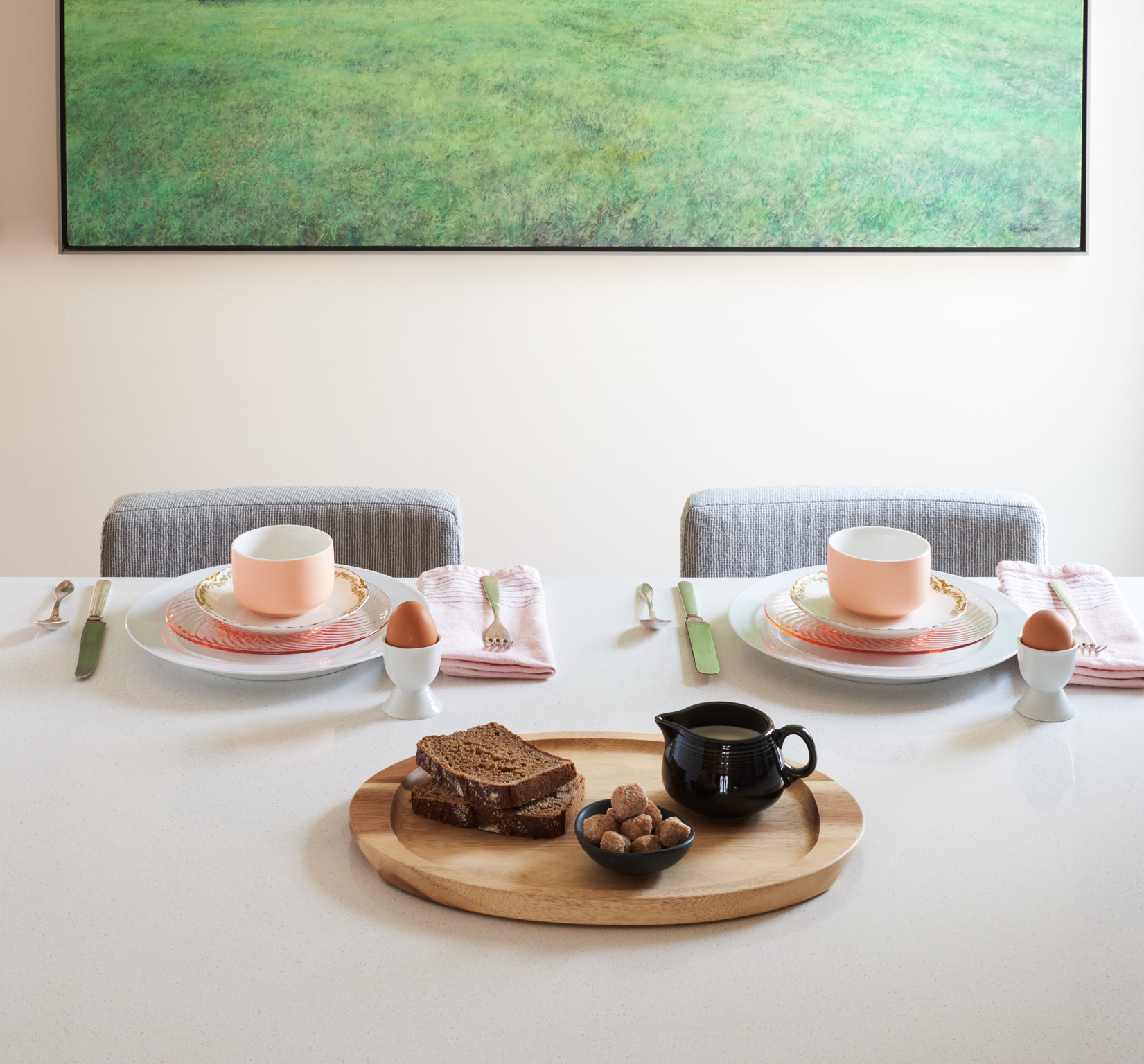 Table set with two plates, cups, and utensils, with a wooden tray holding bread, nuts, and a small teapot.