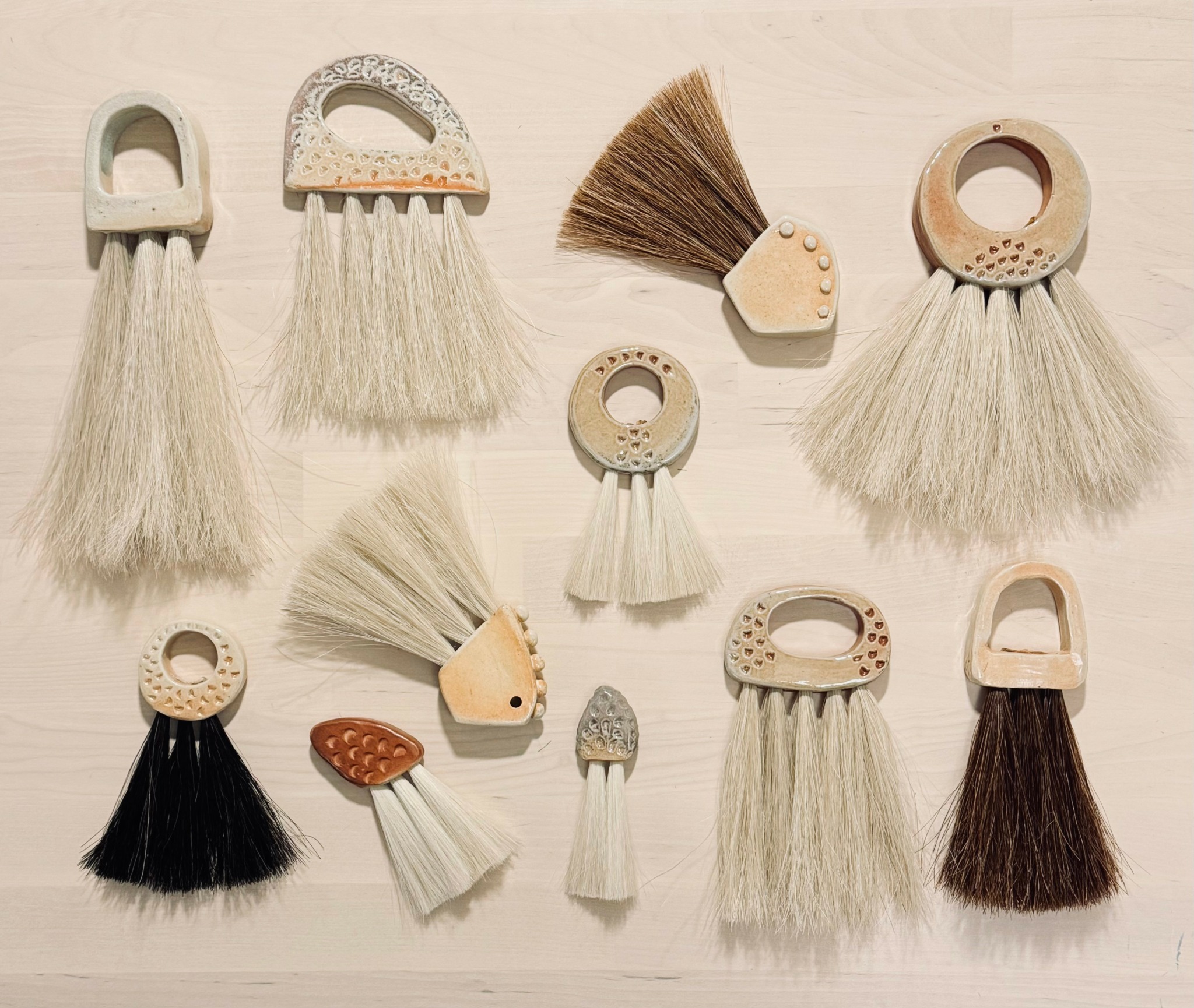 Collection of small brushes and a broom with various handle shapes and bristle colors on a light surface.