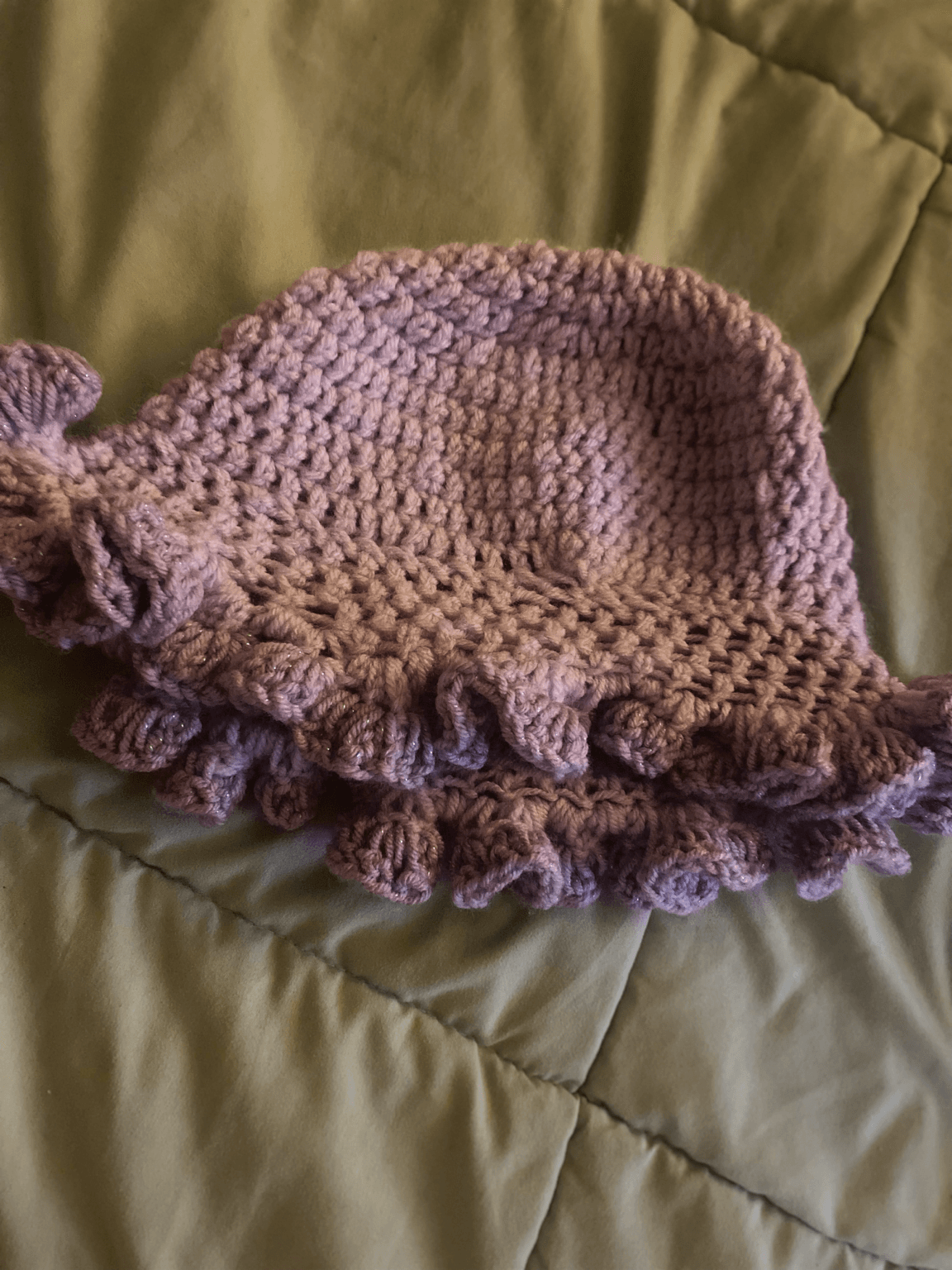 Handmade knitted hat with ruffled edge, placed on a green fabric surface.
