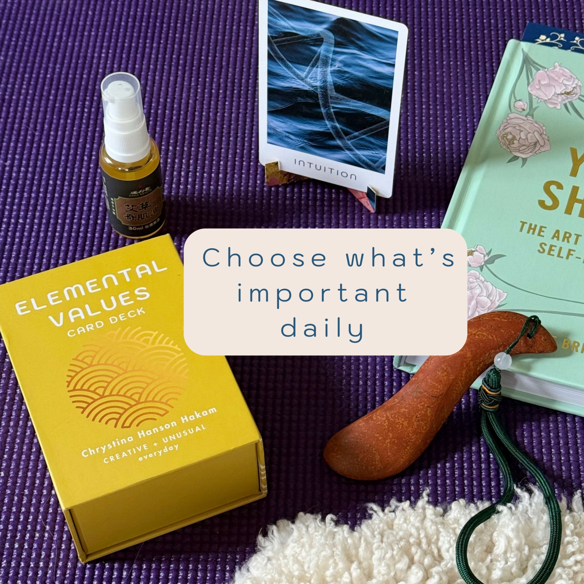 Various items on a purple surface, including a yellow box, a spray bottle, a card deck, a book, and a wooden object.