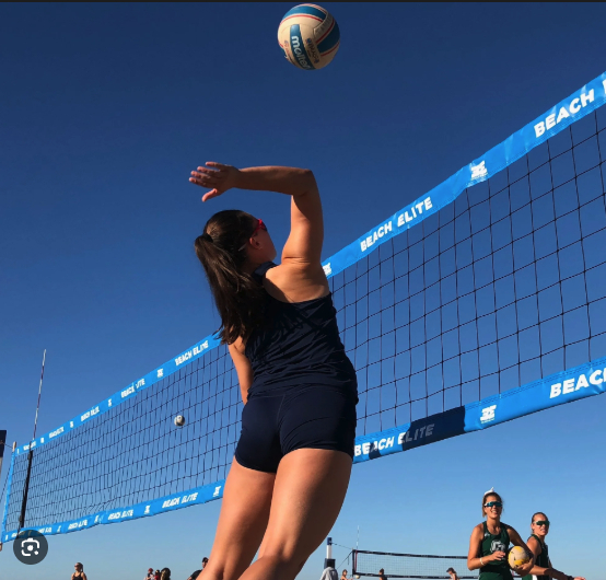 Female volleyball player jumping to hit the ball at the net during a beach volleyball game.