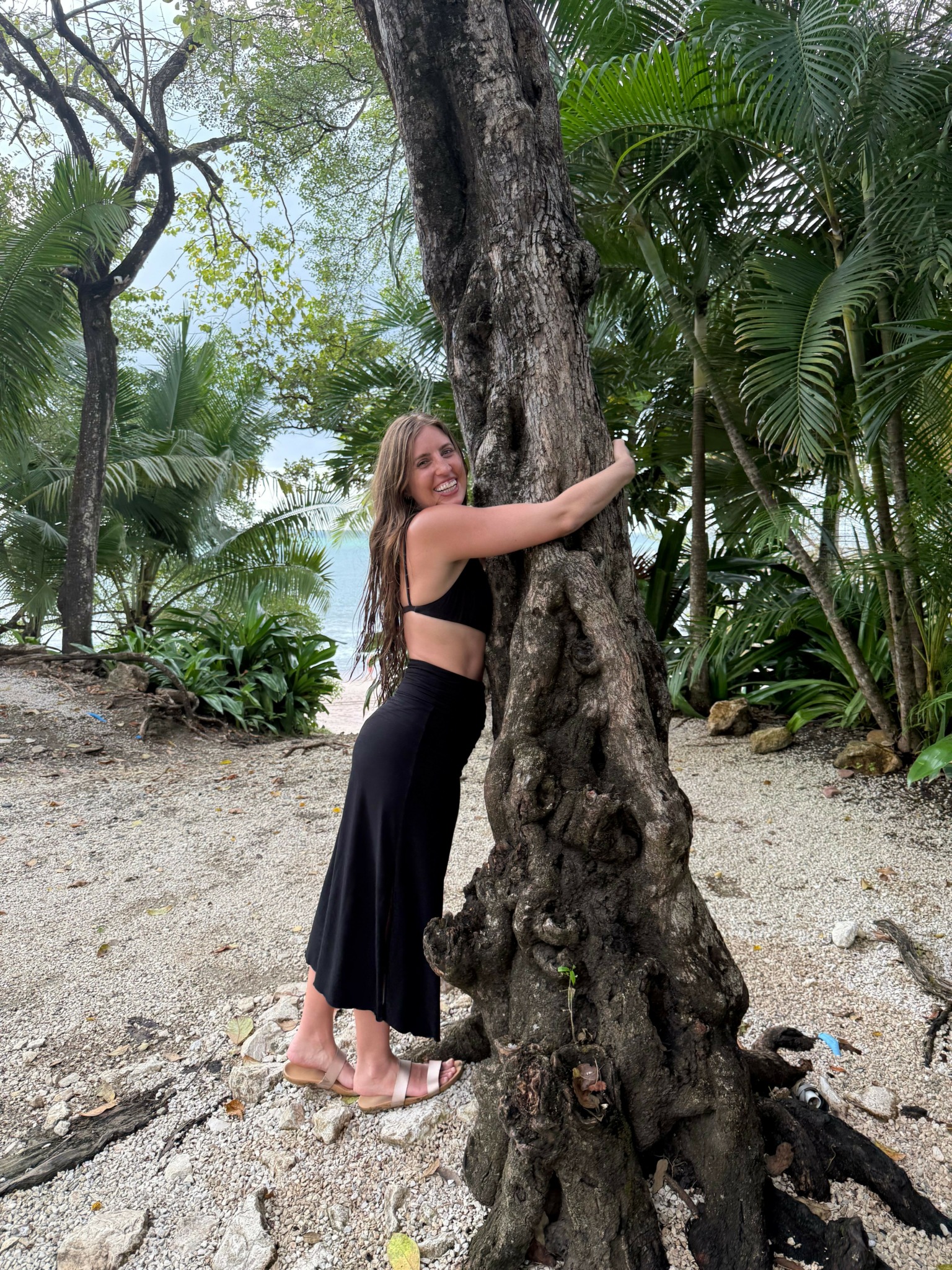Woman hugging a large tree trunk in a tropical forest setting with green foliage.