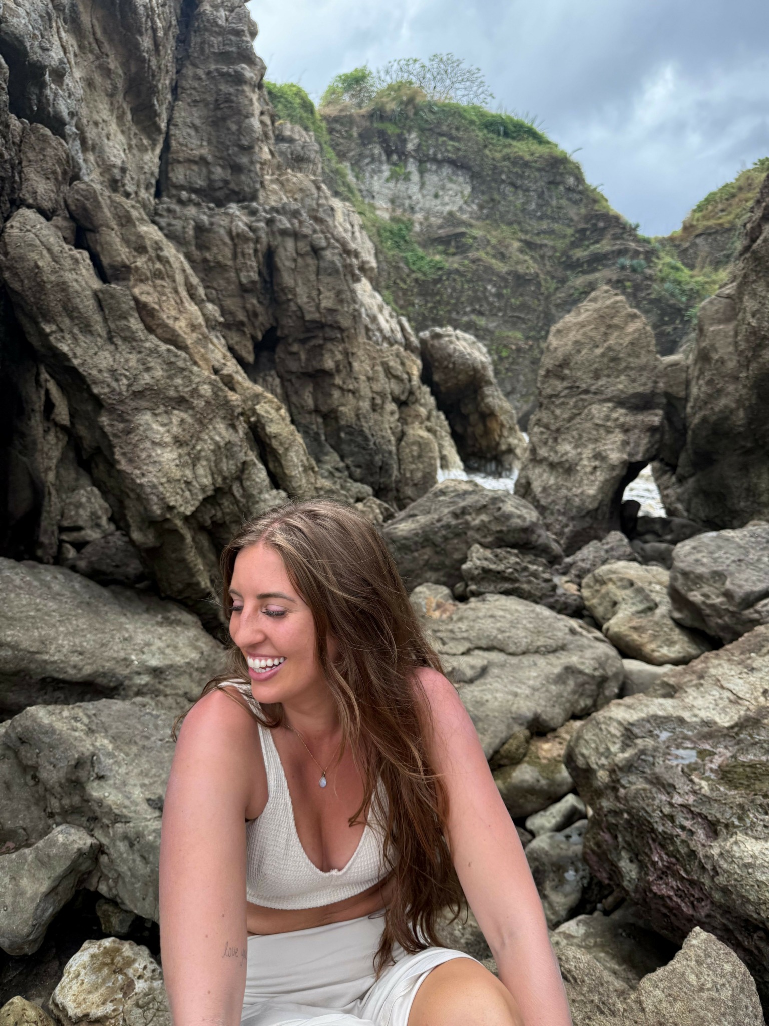 Young woman with long brown hair smiling among large rocks and cliffs outdoors.