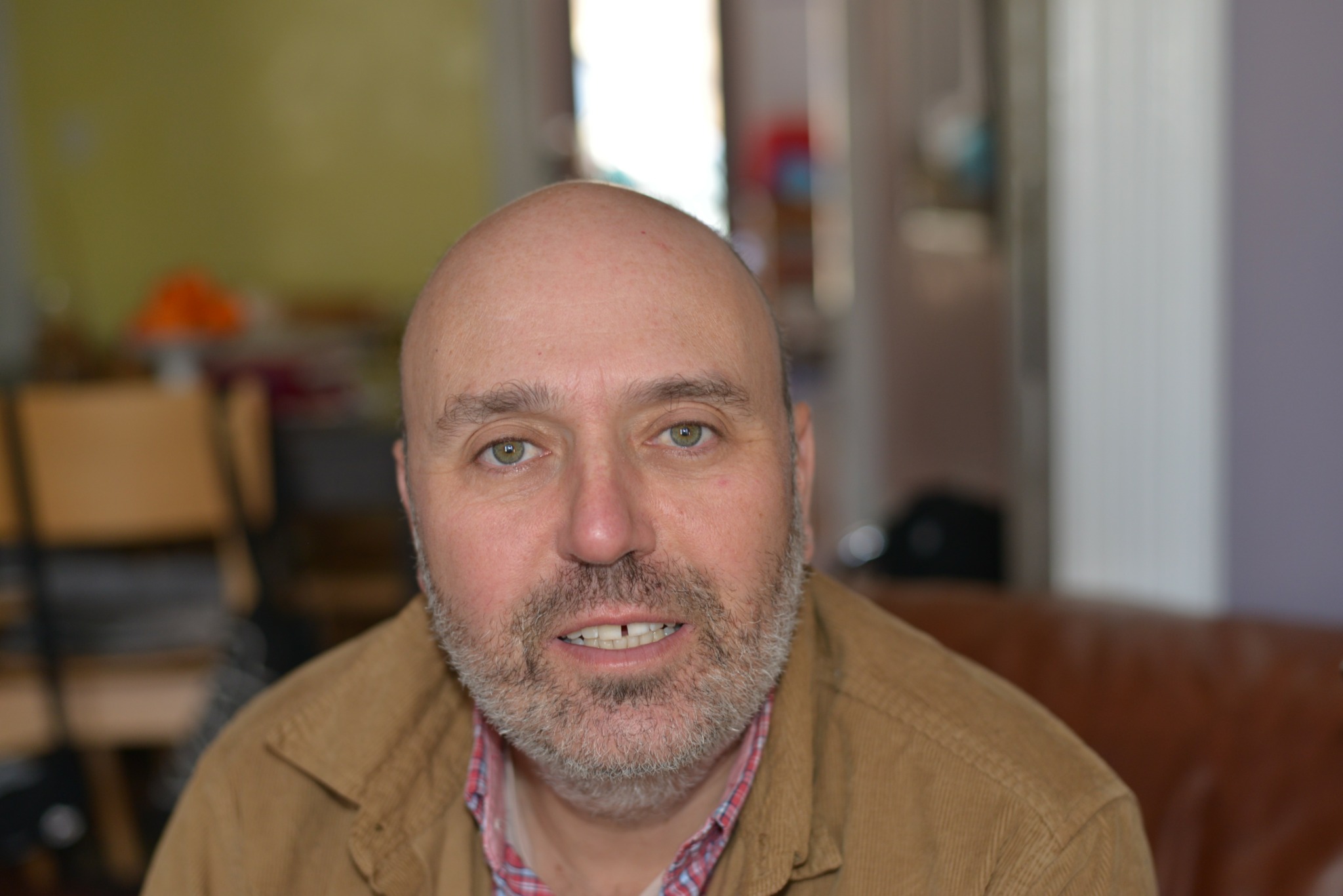 Bald man with beard sitting indoors, looking at the camera.