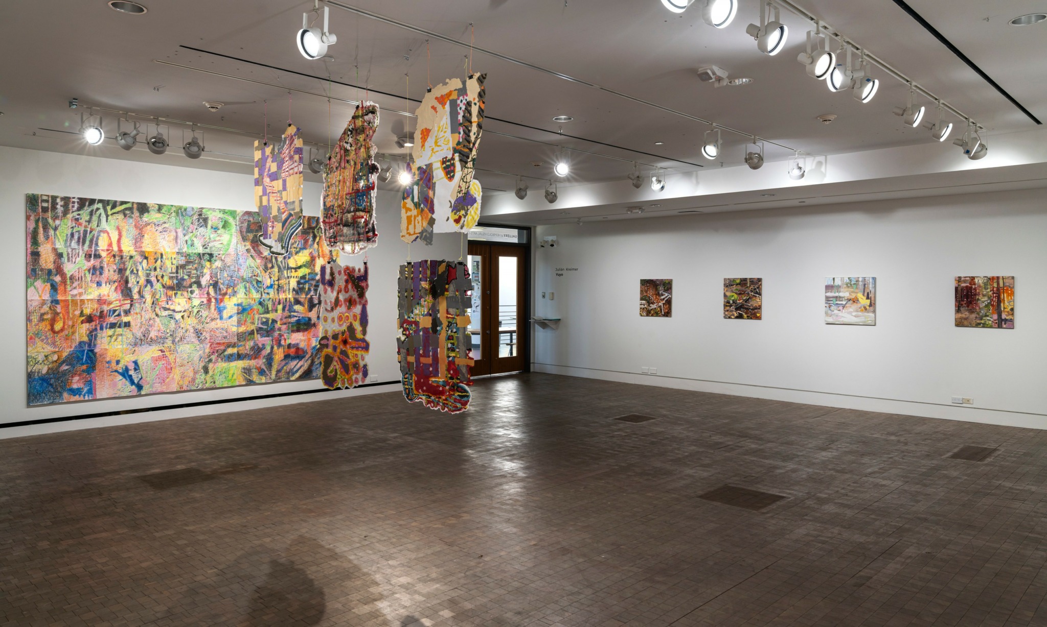 Art gallery with colorful abstract paintings on walls and hanging sculptures in the center.