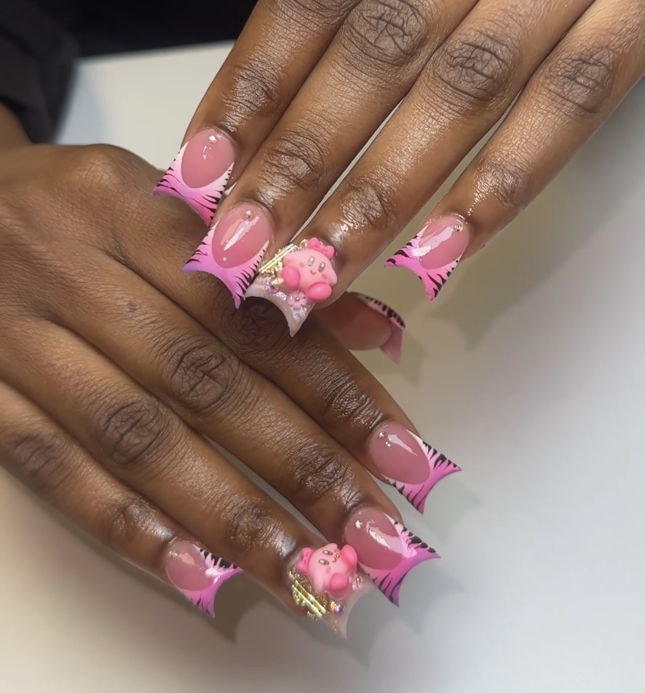 Hands with pink and white decorated nail art, featuring pink bows and gold accents, on a white surface.
